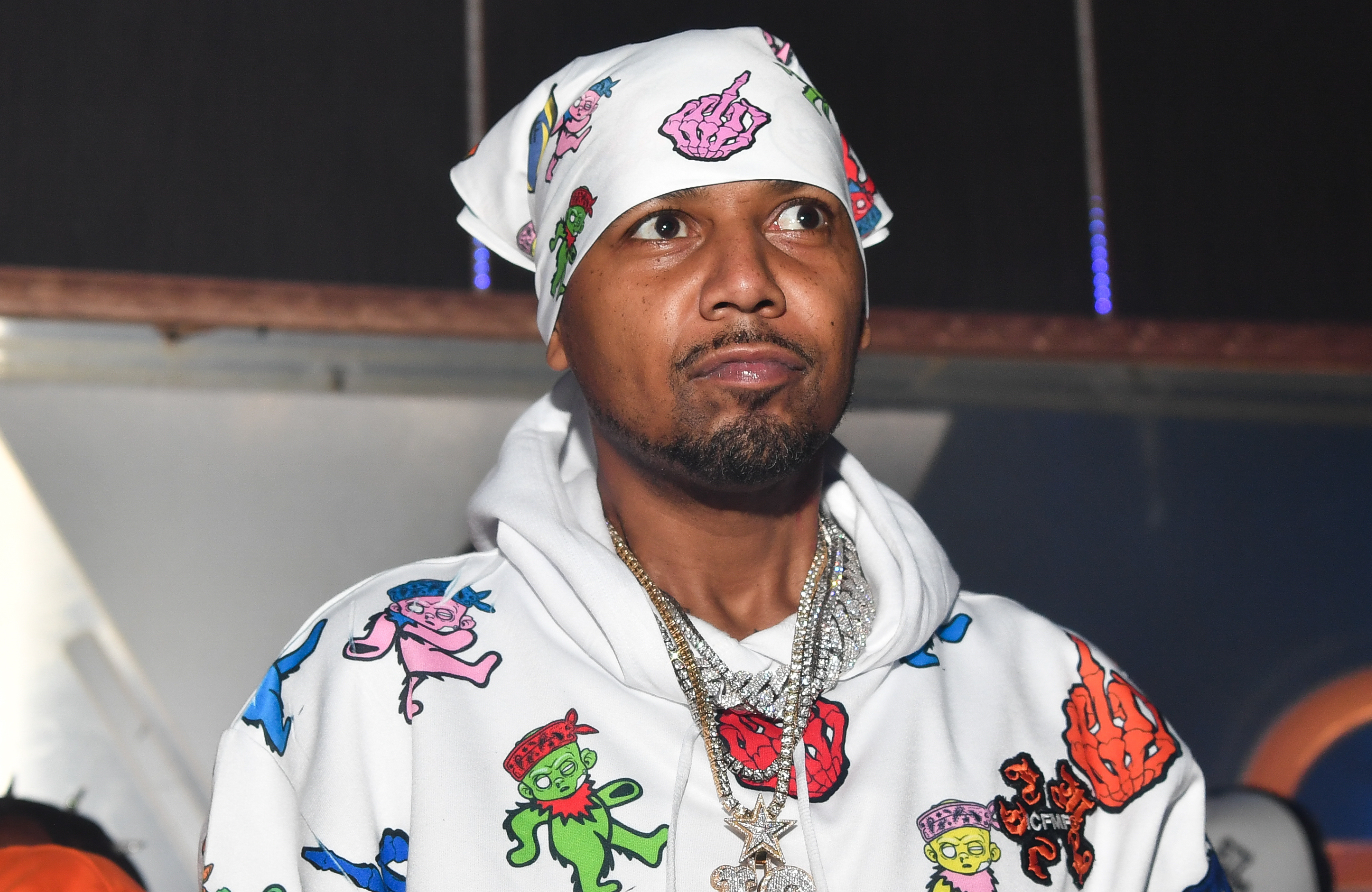 Juelz Santana wearing a colorful hoodie with cartoon designs and a matching bandana, accessorized with multiple necklaces.