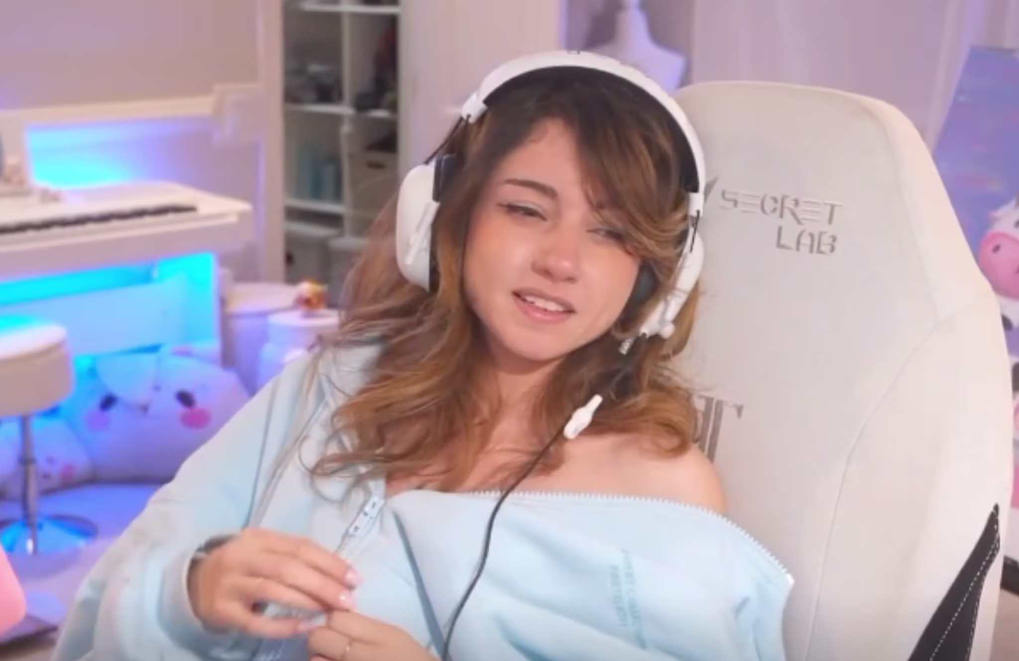 Bonnie with headphones sits in a gaming chair, wearing a light blue top. The room has soft lighting and gaming accessories.
