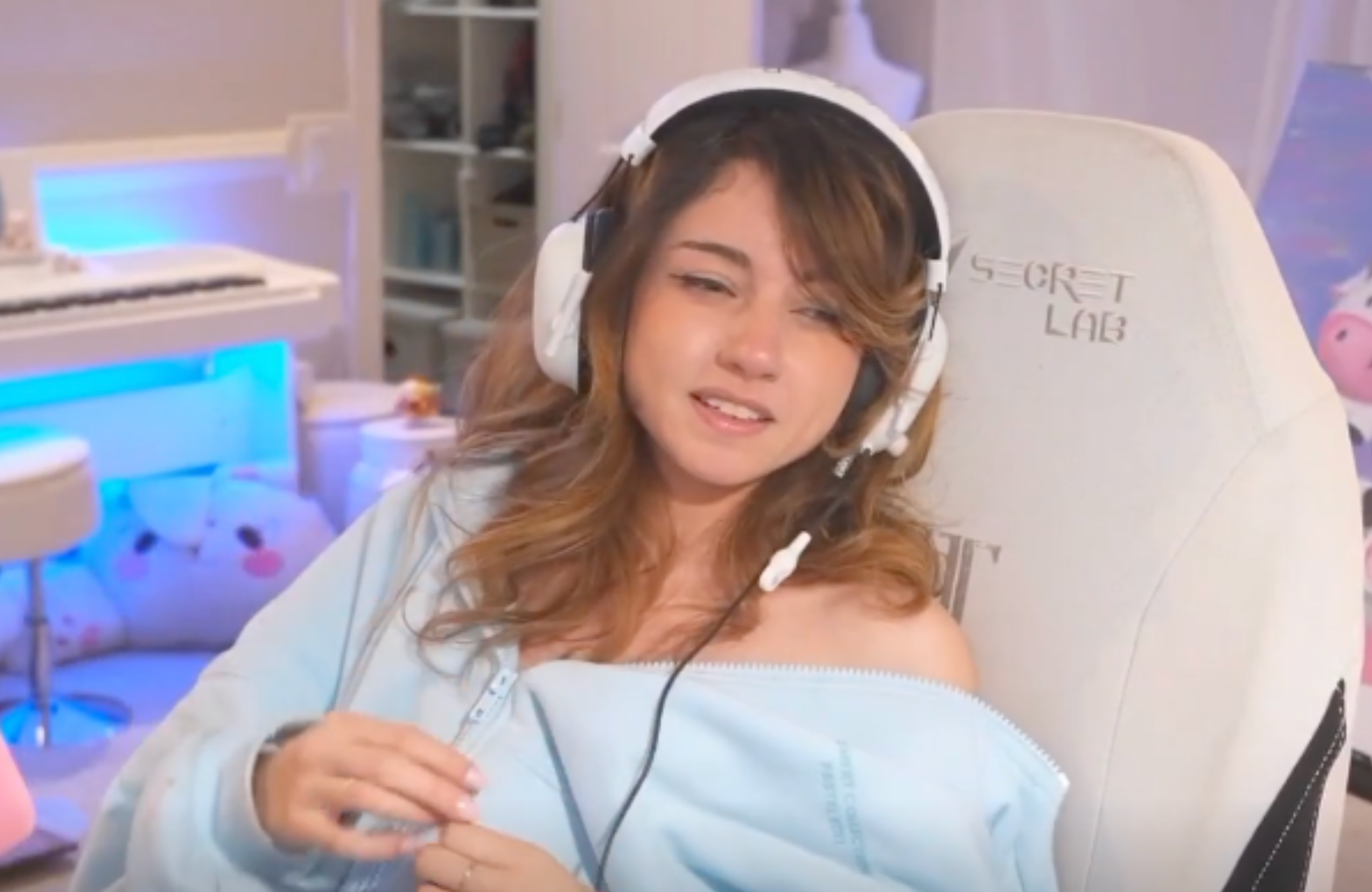 Bonnie with headphones sits in a gaming chair, wearing a light blue hoodie, in a room with pastel decor.