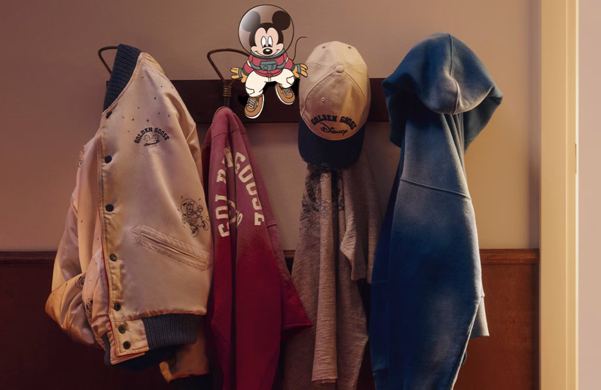 A coat rack with jackets, a cap, and a hoodie hanging. A Mickey Mouse figure is on the wall above.