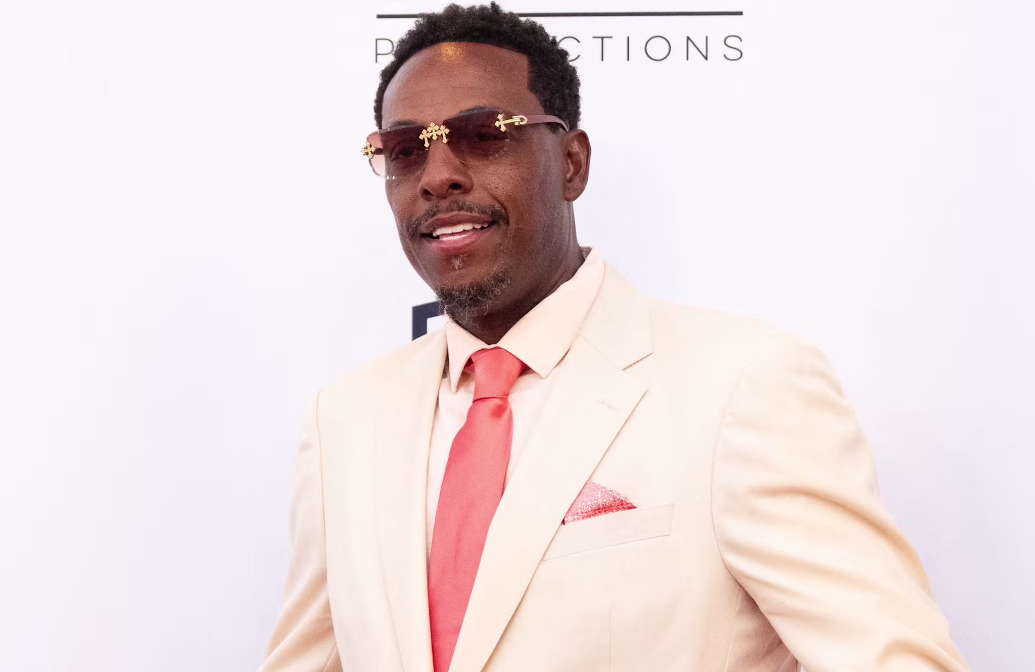 Paul Pierce in a cream suit with a coral tie and pocket square poses on a red carpet. 