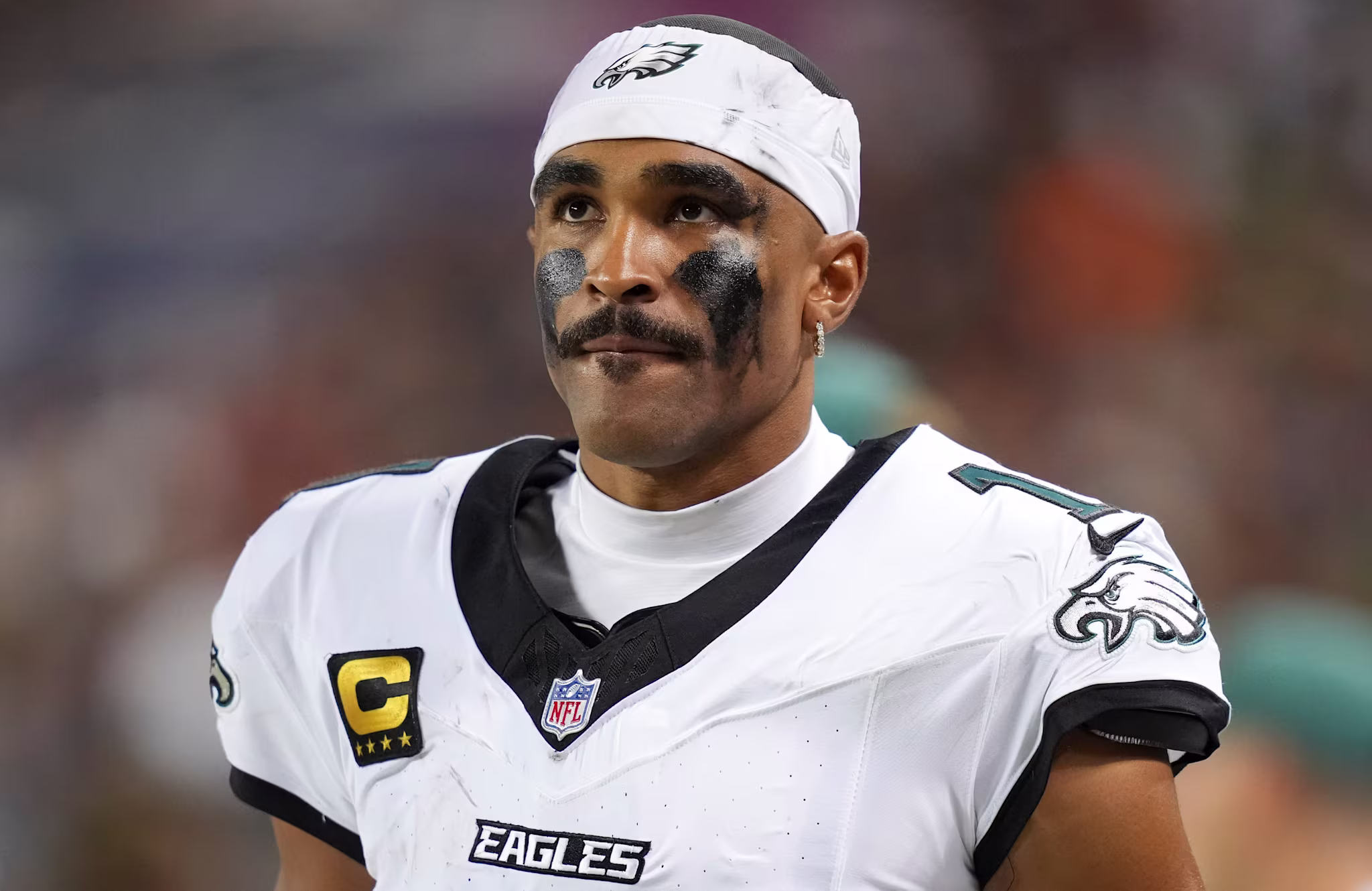 NFL player Jalen Hurts in a Philadelphia Eagles uniform, wearing eye black and a headband, looking focused.
