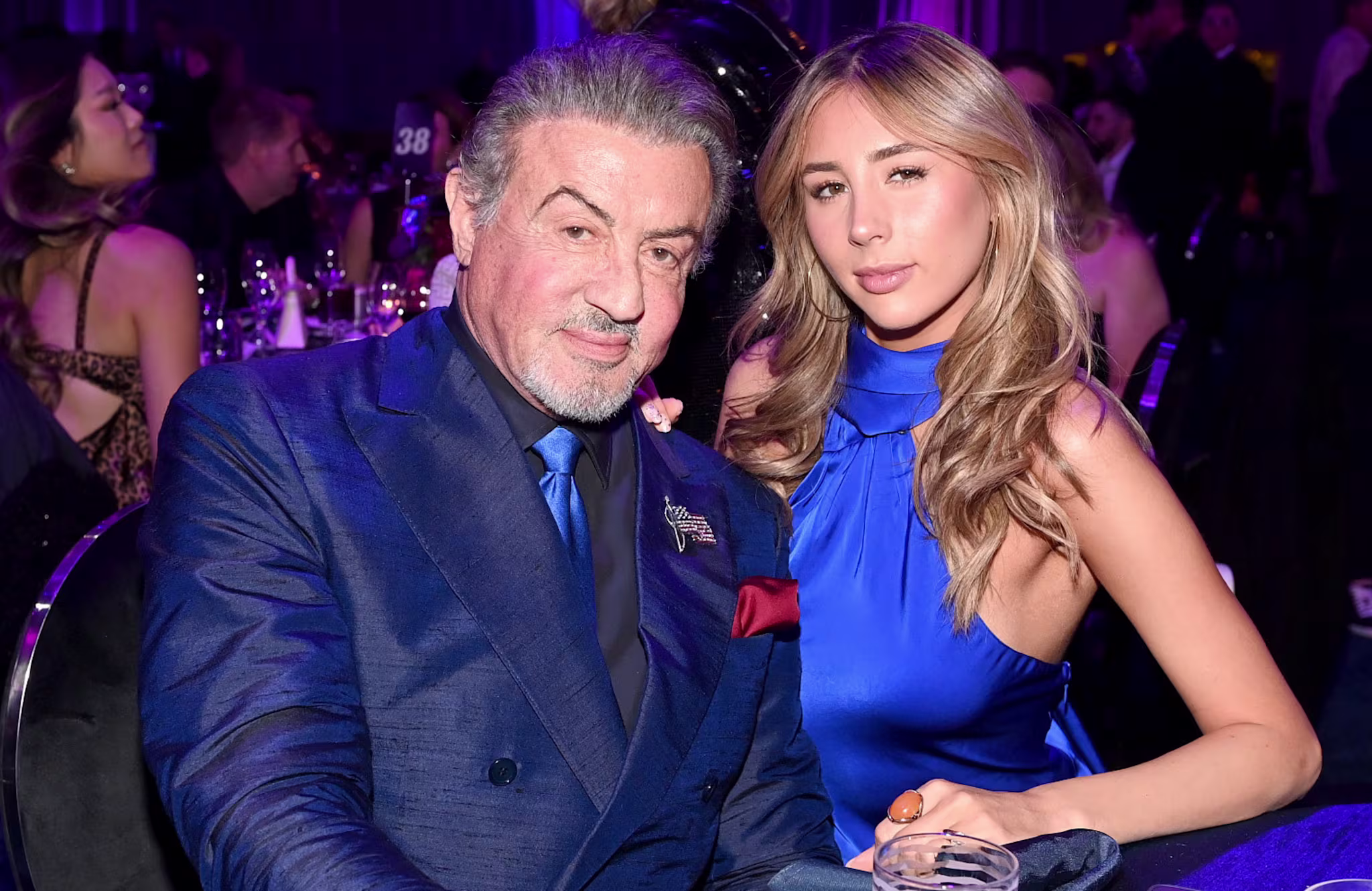 Sylvester Stallone in a blue suit sits with Scarlet Rose Stallone in a blue dress at a formal event.