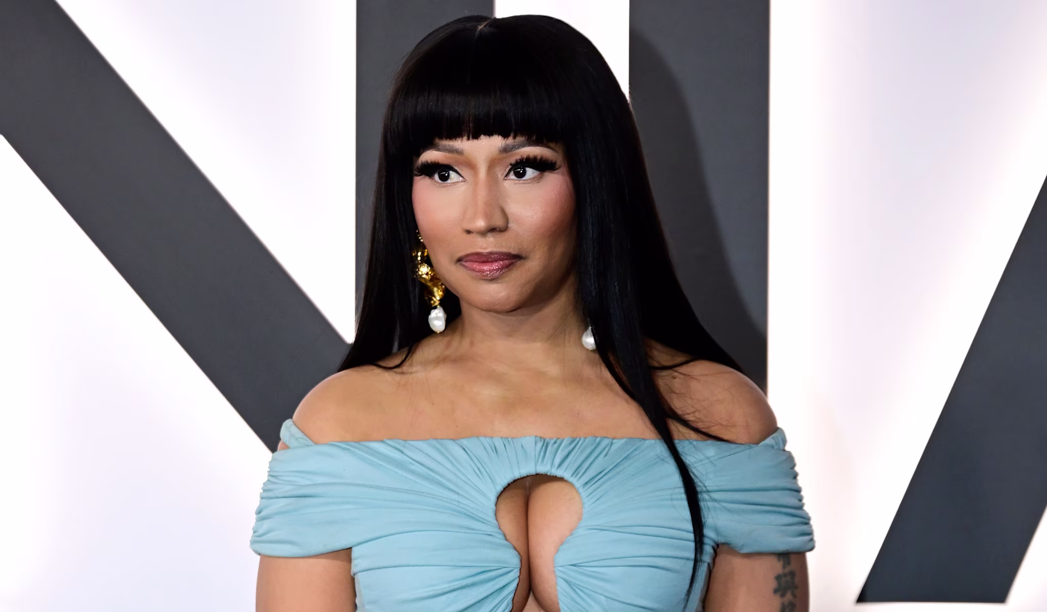 Nicki Minaj in a blue off-shoulder dress with gold bracelets, posing at an event.
