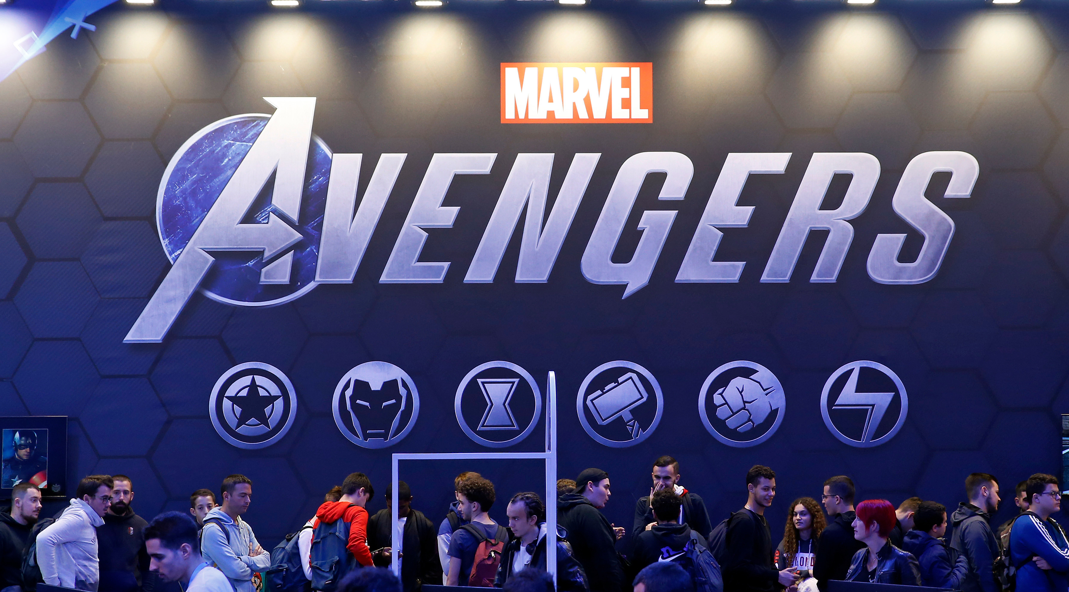 People at a Marvel Avengers event, featuring a large logo and superhero symbols on display.