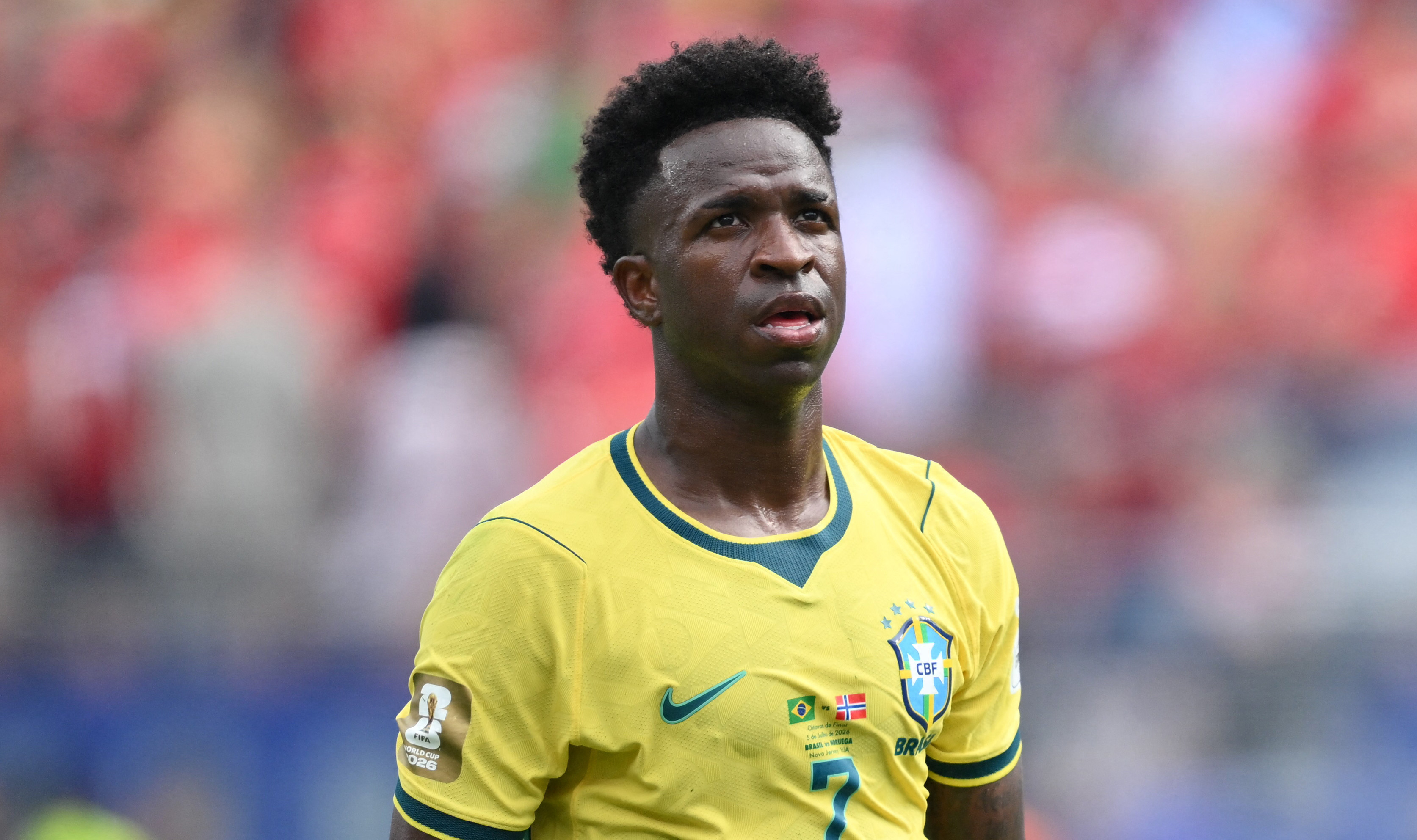 Vinícius Júnior a yellow Brazil jersey on the field, with a blurred crowd in the background.