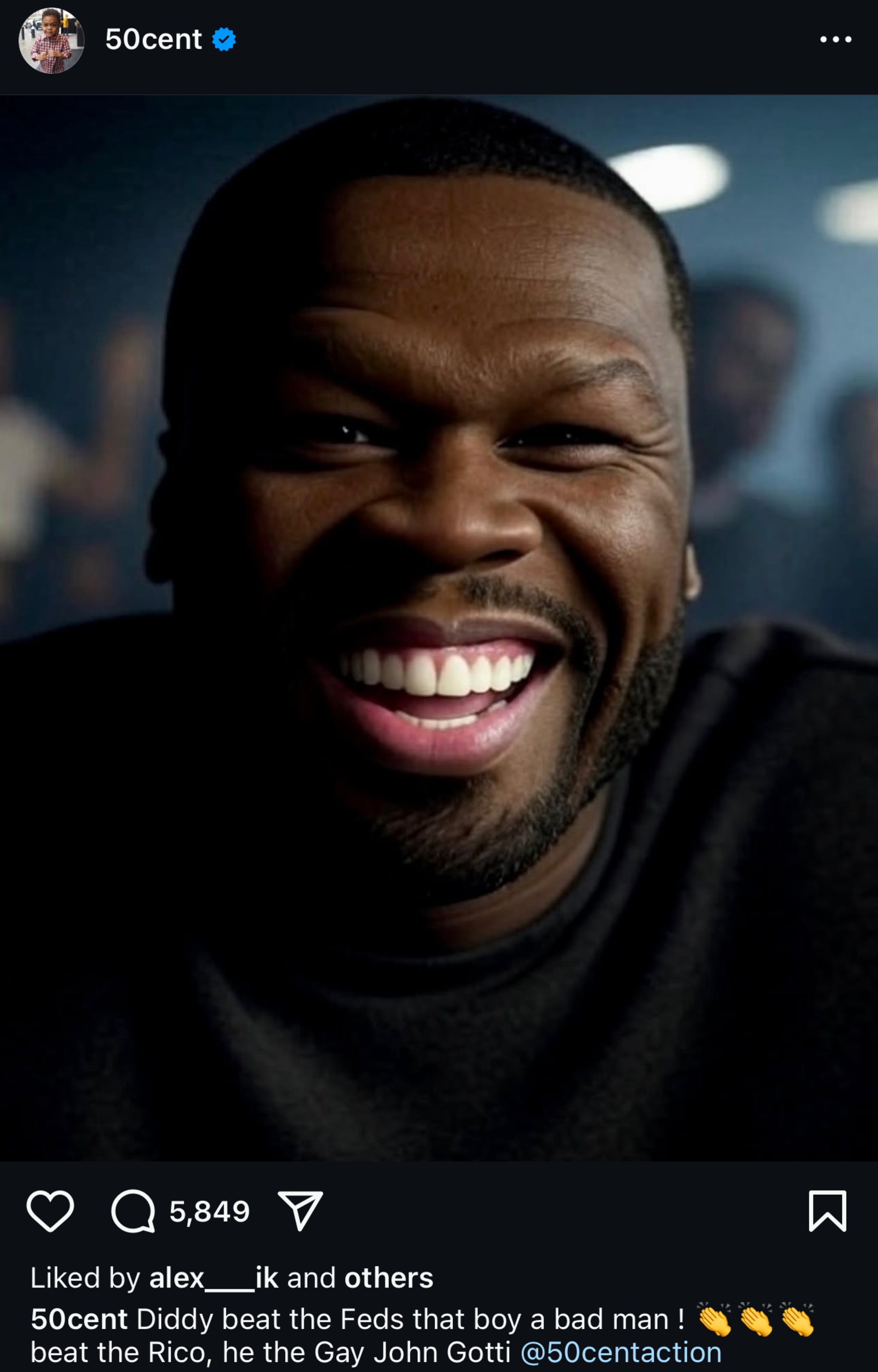 Rapper 50 Cent is smiling broadly, wearing a dark shirt. The background is blurred.