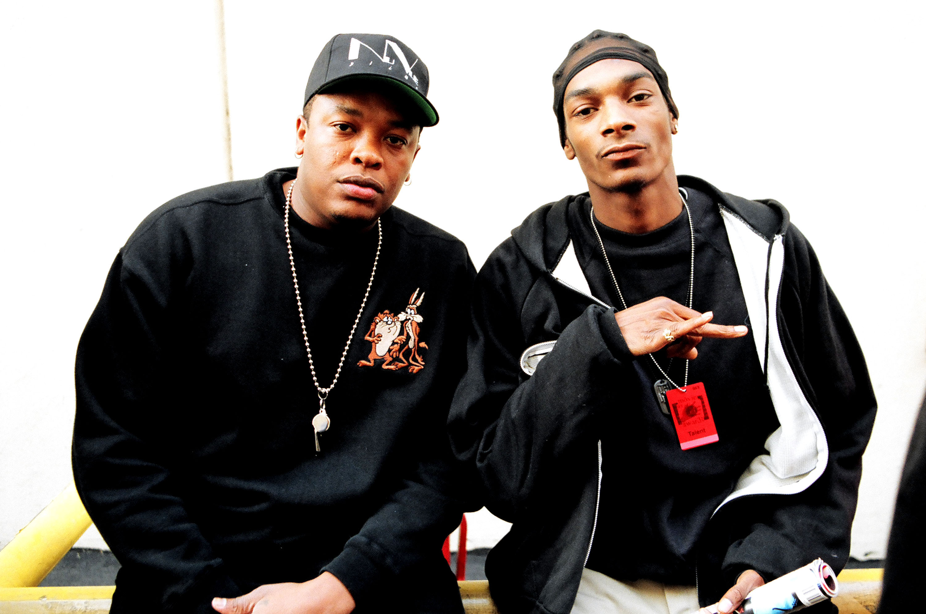 Dr. Dre and Snoop Dogg posing together, both wearing casual black clothing and hats.