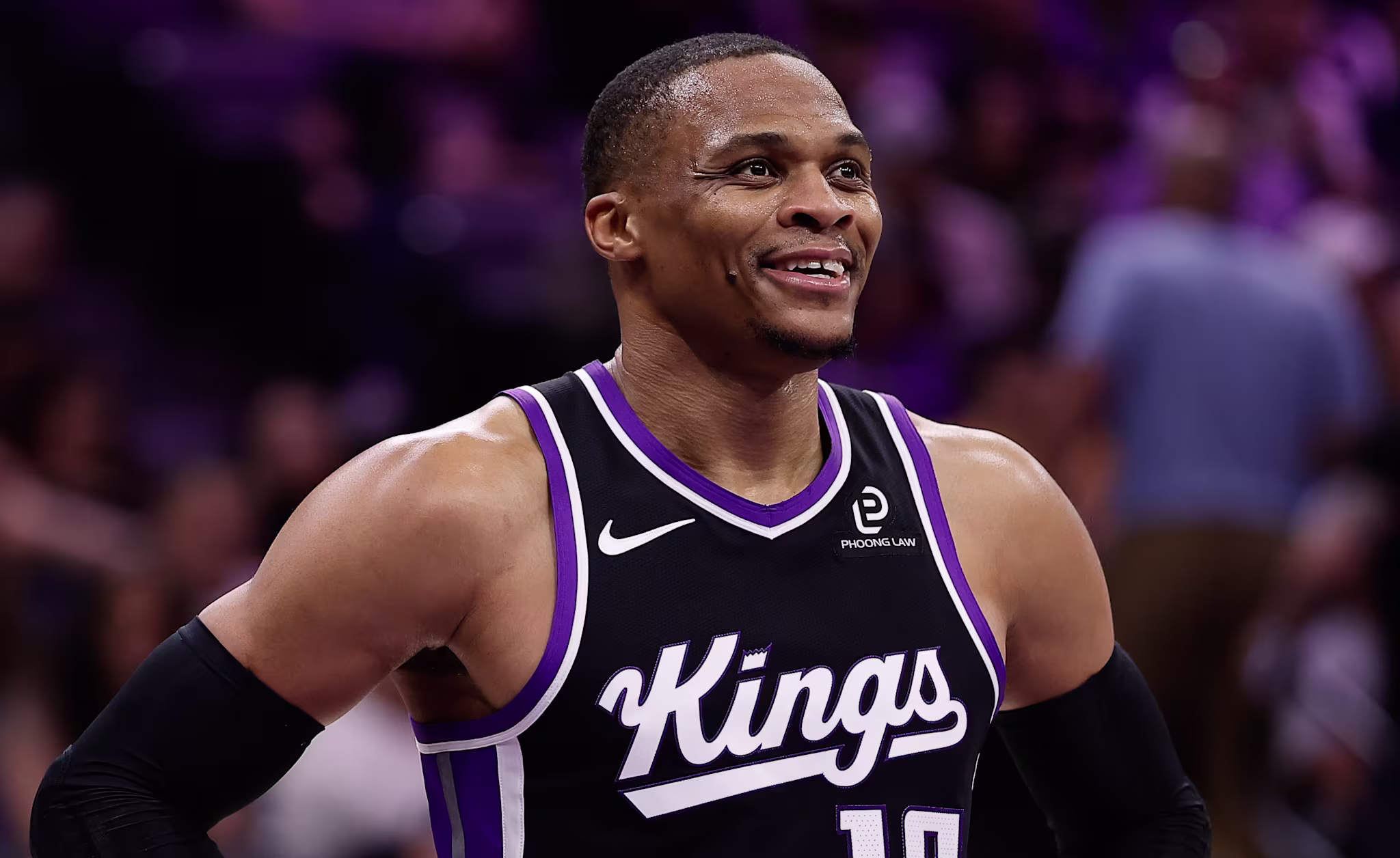Russell Westbrook in a Sacramento Kings uniform, number 18, smiling with hands on hips during a game.