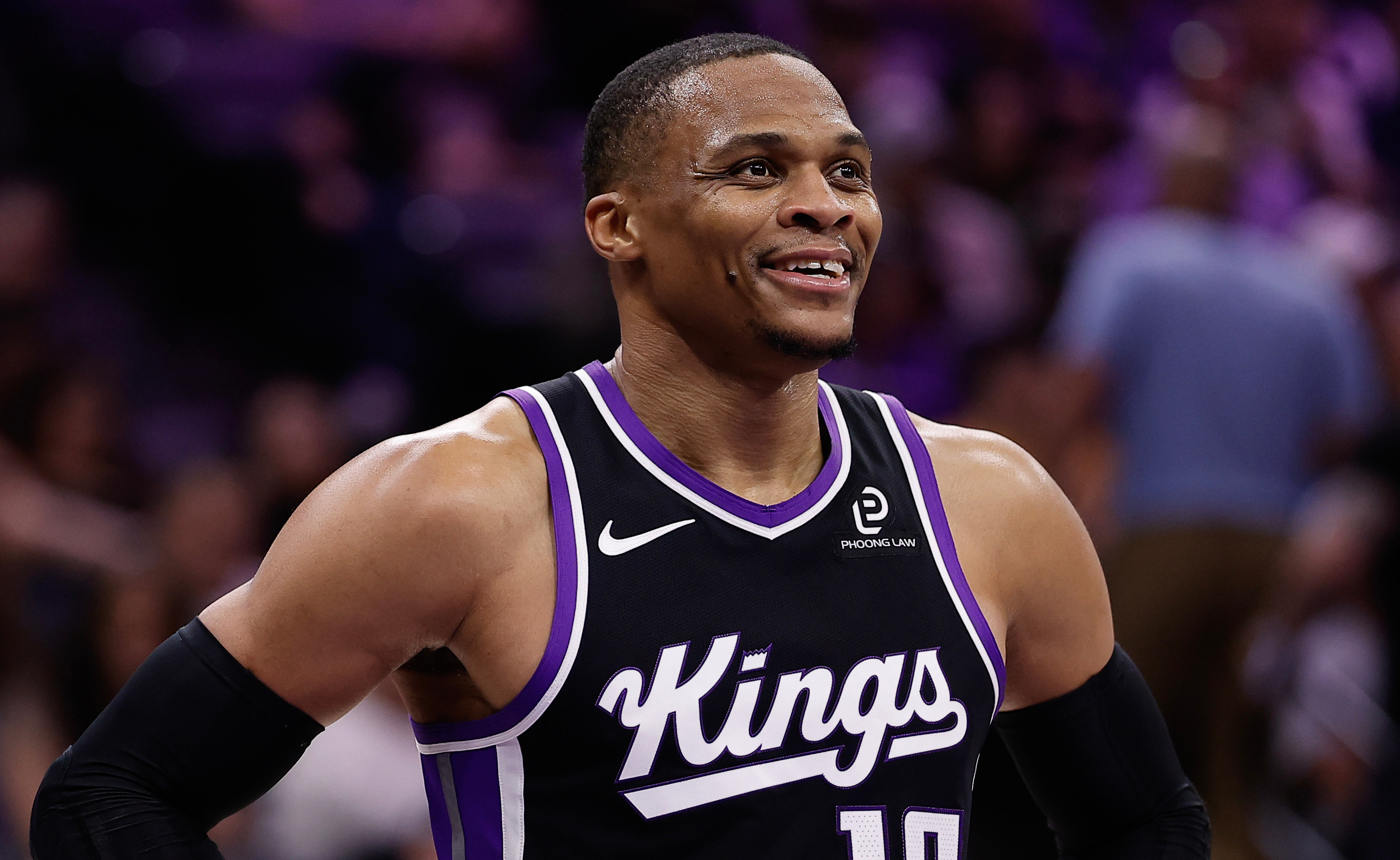 Russell Westbrook in a Sacramento Kings uniform, number 18, smiling with hands on hips during a game.