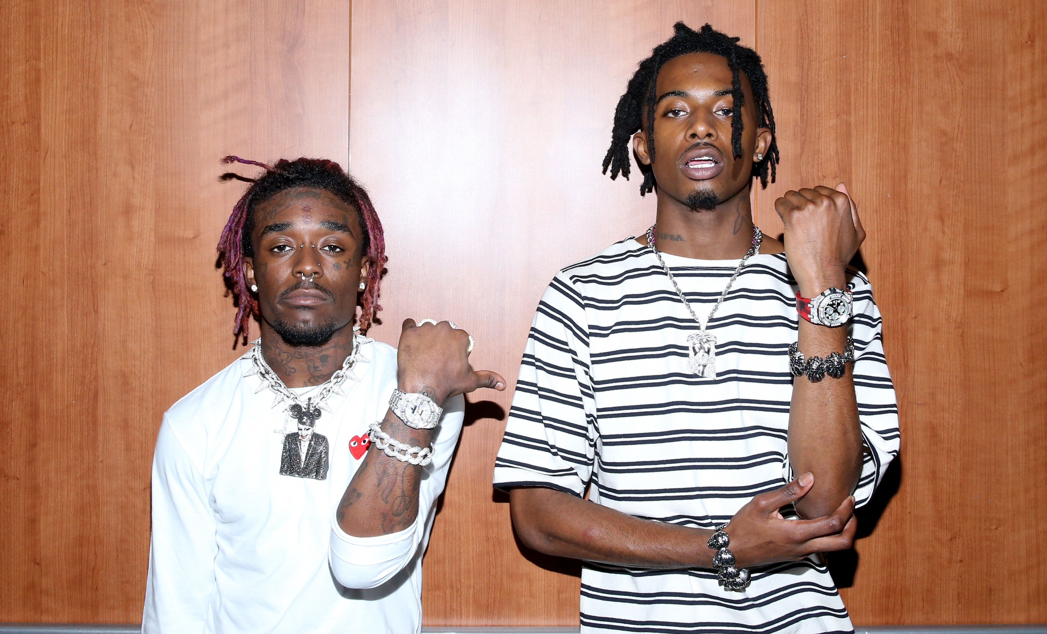 Lil Uzi Vert and Playboi Carti pose together, showcasing jewelry, against a wooden backdrop.