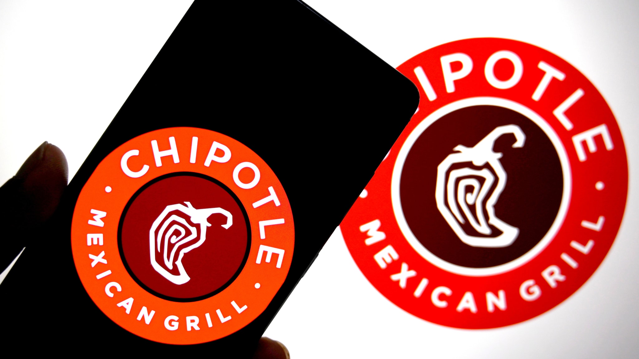 In this photo illustration, the Chipotle logo is seen displayed on a smartphone and in the background. 