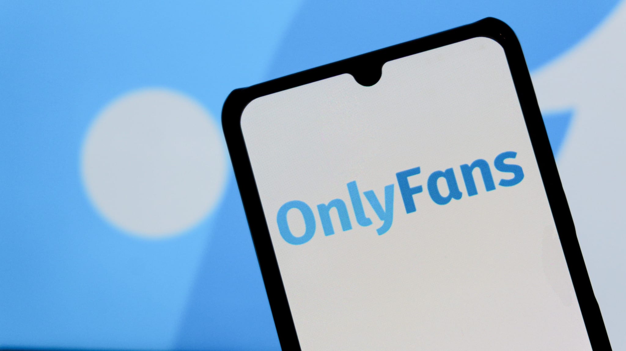 In this photo illustration, the OnlyFans logo is seen displayed on a mobile phone and in the background.
