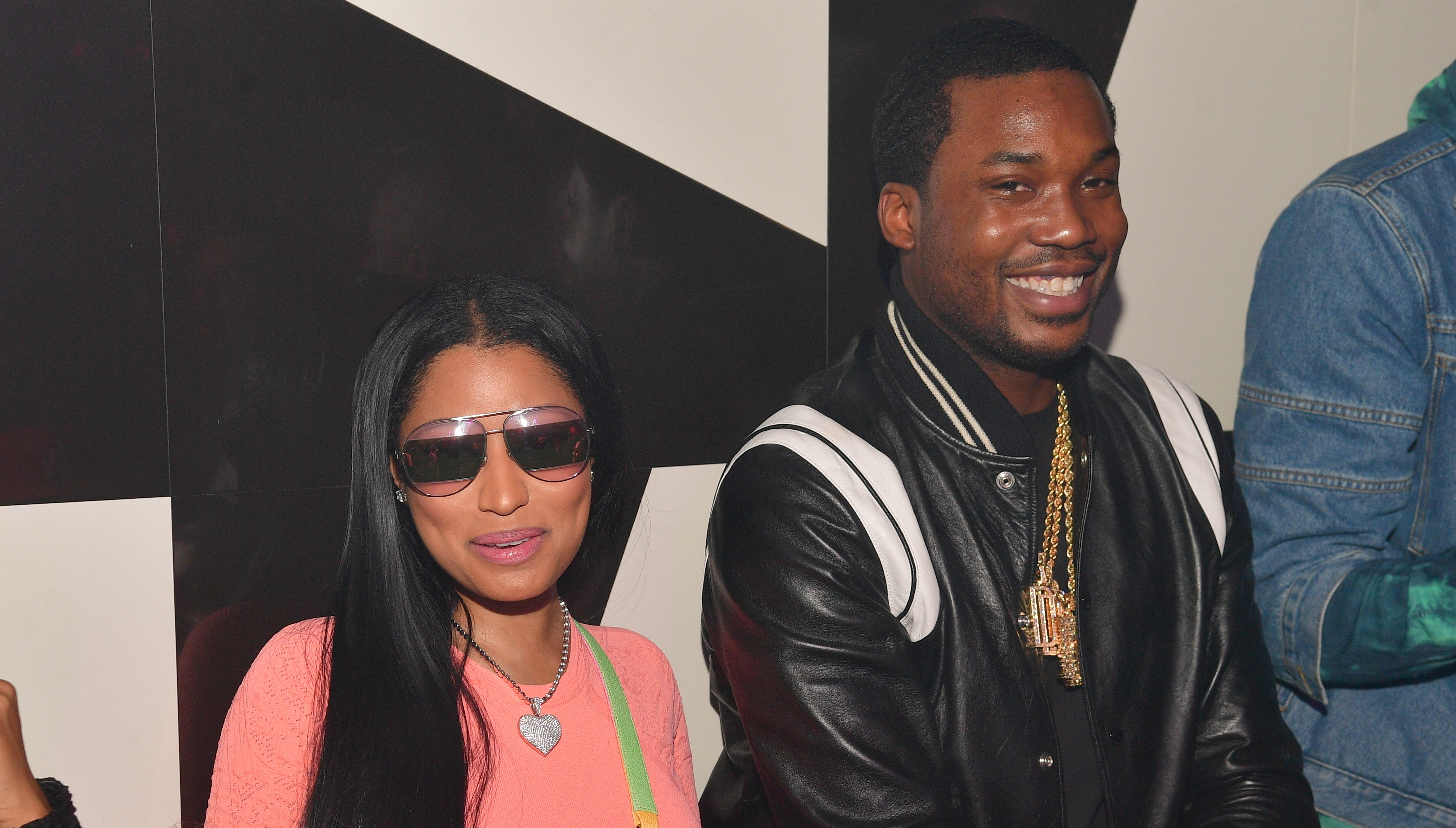 Nicki Minaj in sunglasses and pink outfit, sitting beside Meek Mill in a black jacket, both smiling at an event.