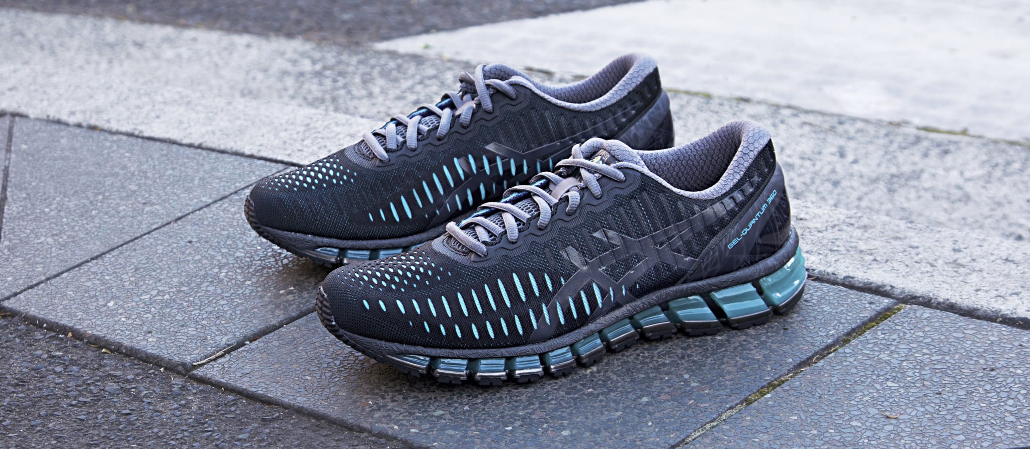 A pair of black and blue Gel Quantum 360s with a sleek design, placed on a textured pavement.