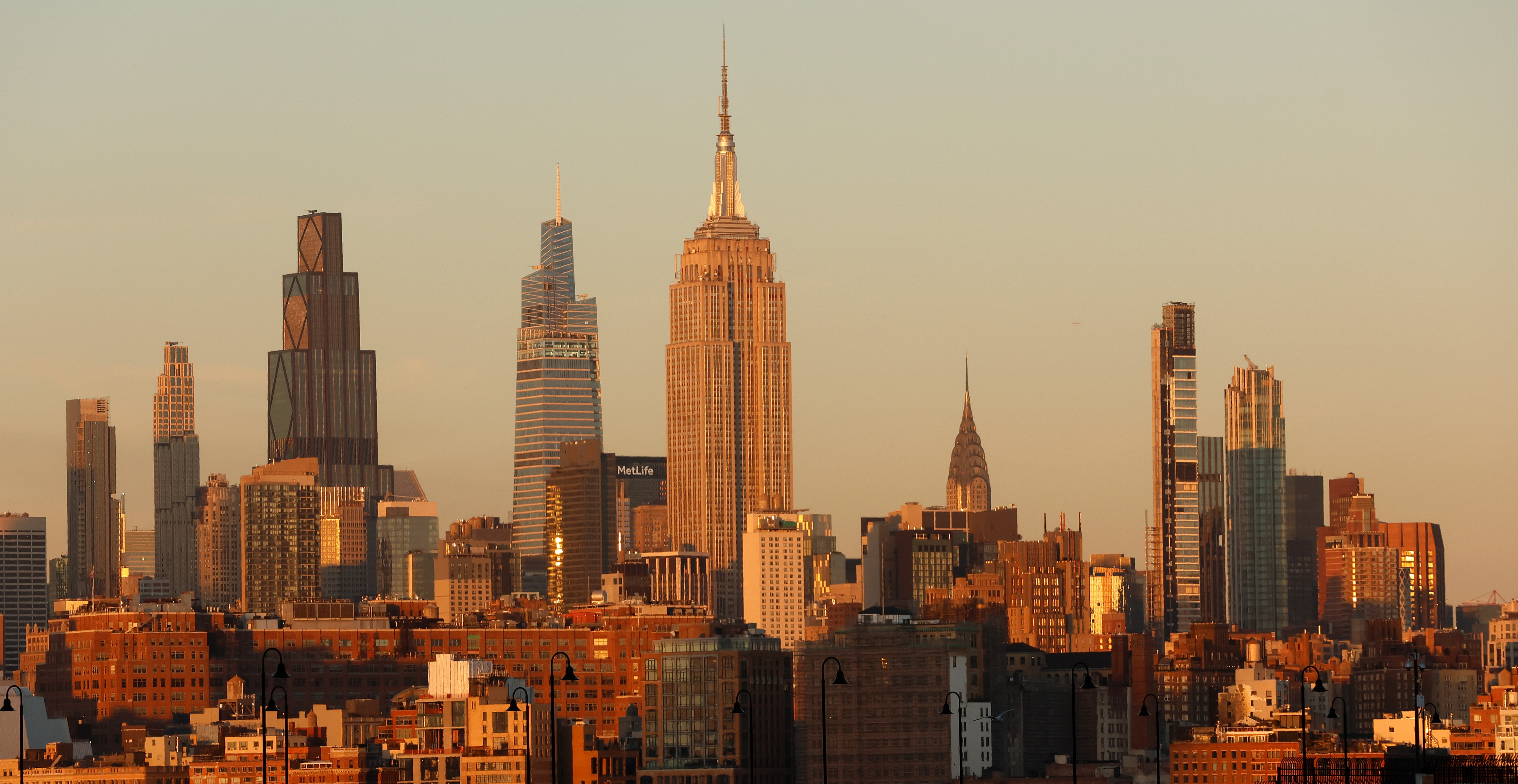 New York City skyline at sunset, featuring the Empire State Building and surrounding skyscrapers bathed in golden light.
