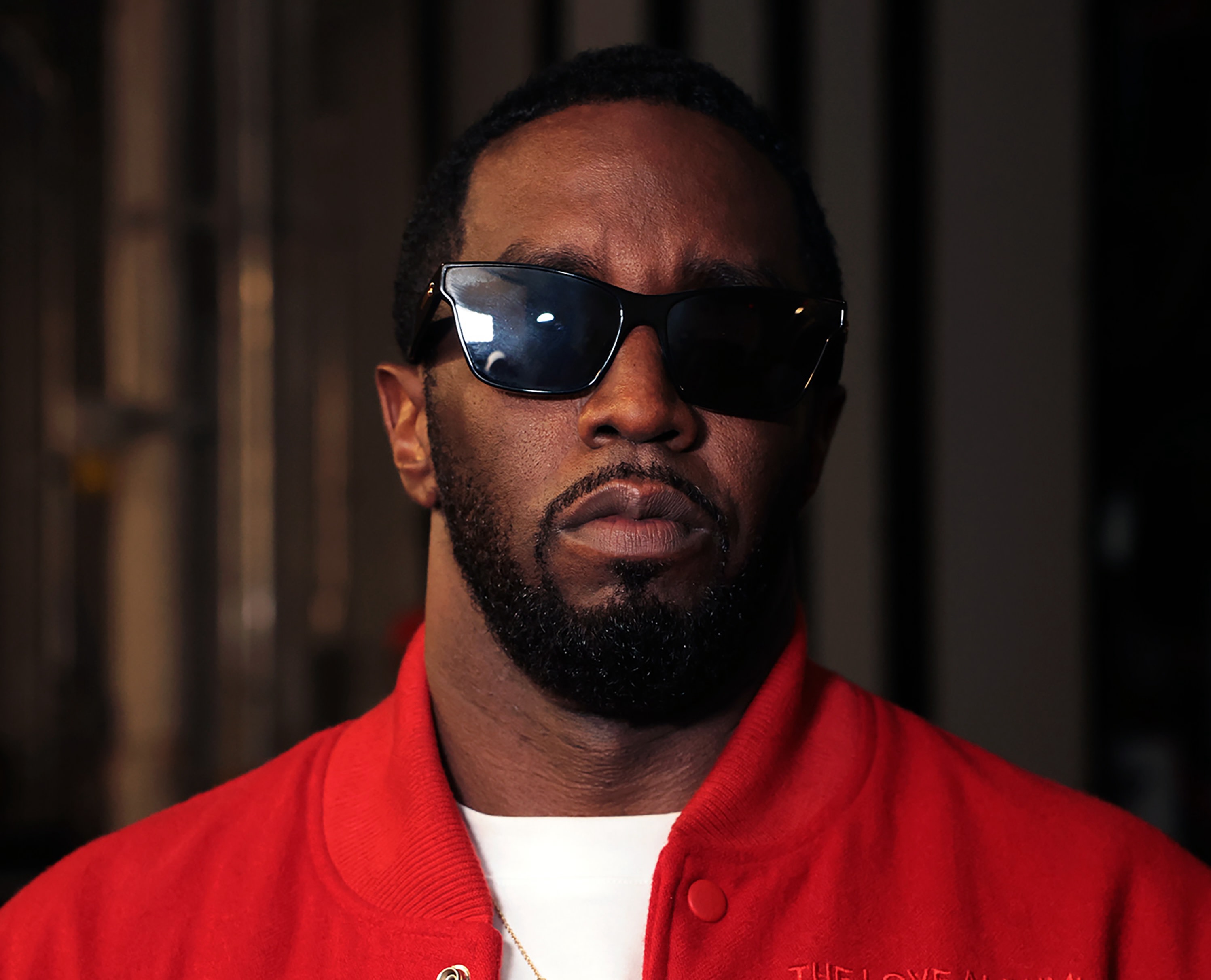 Diddy wearing sunglasses and a red jacket, looking directly at the camera.