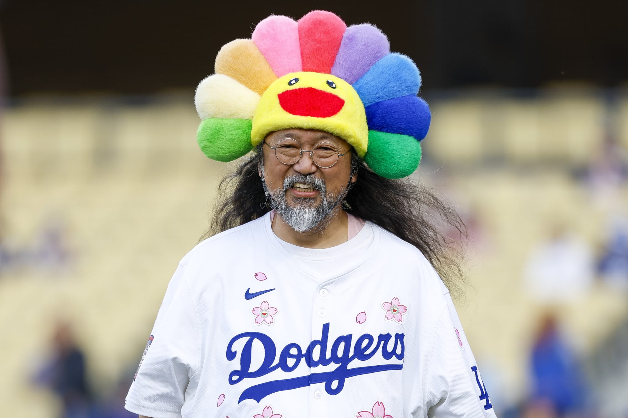 A person wearing a Dodgers jersey and a colorful flower hat with a smiley face, standing in a stadium.