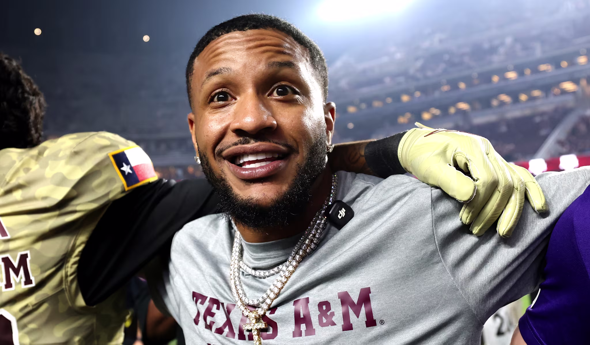 Bendadonnn and a group of Texas A&M football players and staff celebrate on the field, smiling and embracing each other under stadium lights.