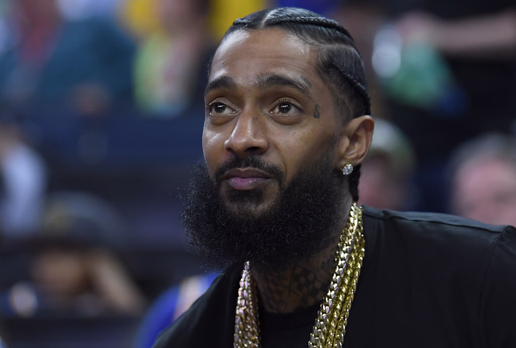 Rapper Nipsey Hussle sitting at courtside looks on during an NBA basketball game between the Milwaukee Bucks and Golden State Warriors at ORACLE Arena on March 29, 2018 in Oakland, California. NOTE TO USER: User expressly acknowledges and agrees that, by downloading and or using this photograph, User is consenting to the terms and conditions of the Getty Images License Agreement. 