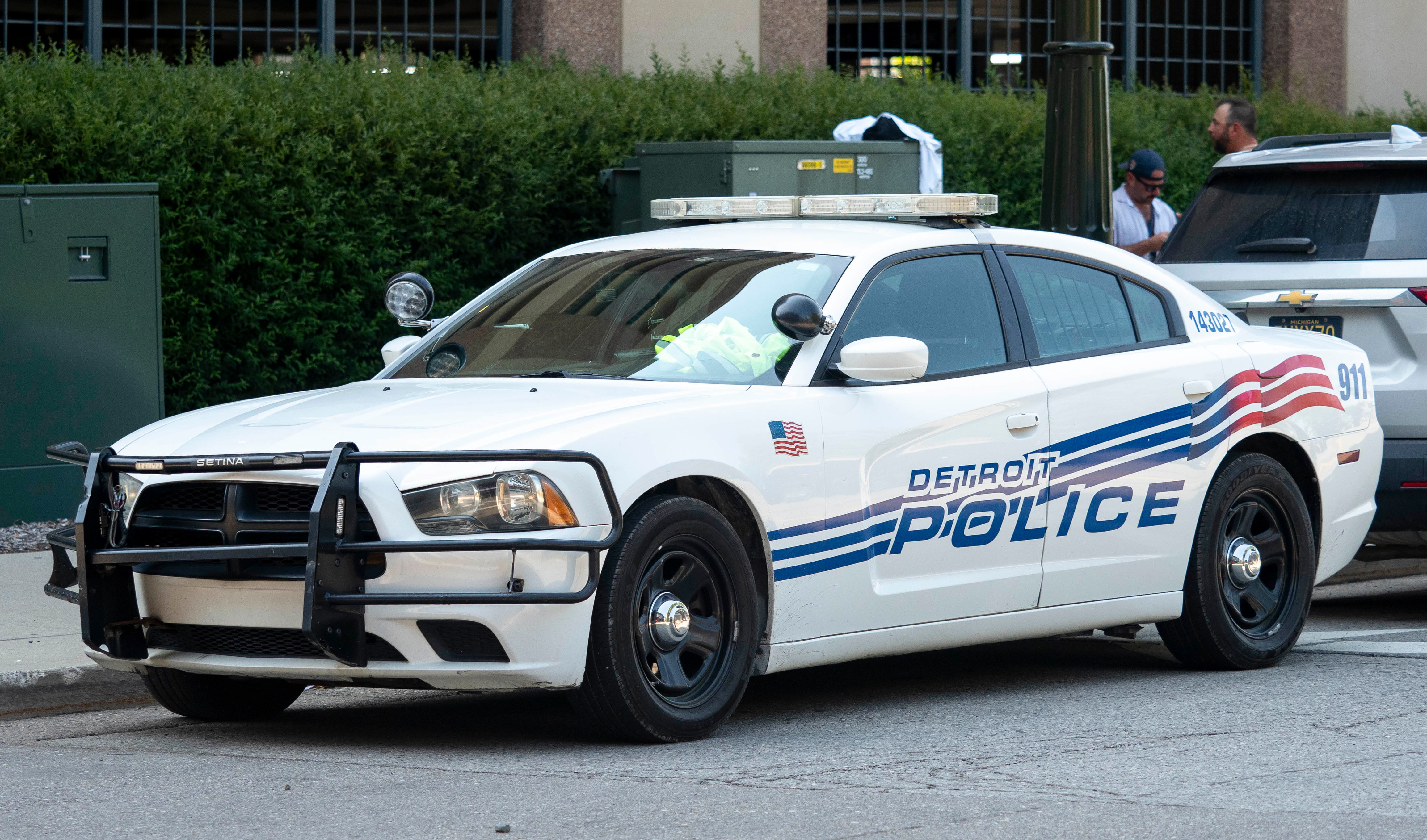 A Detroit Police car parked on the street, featuring a white body with blue and red stripes, and a front push bumper.