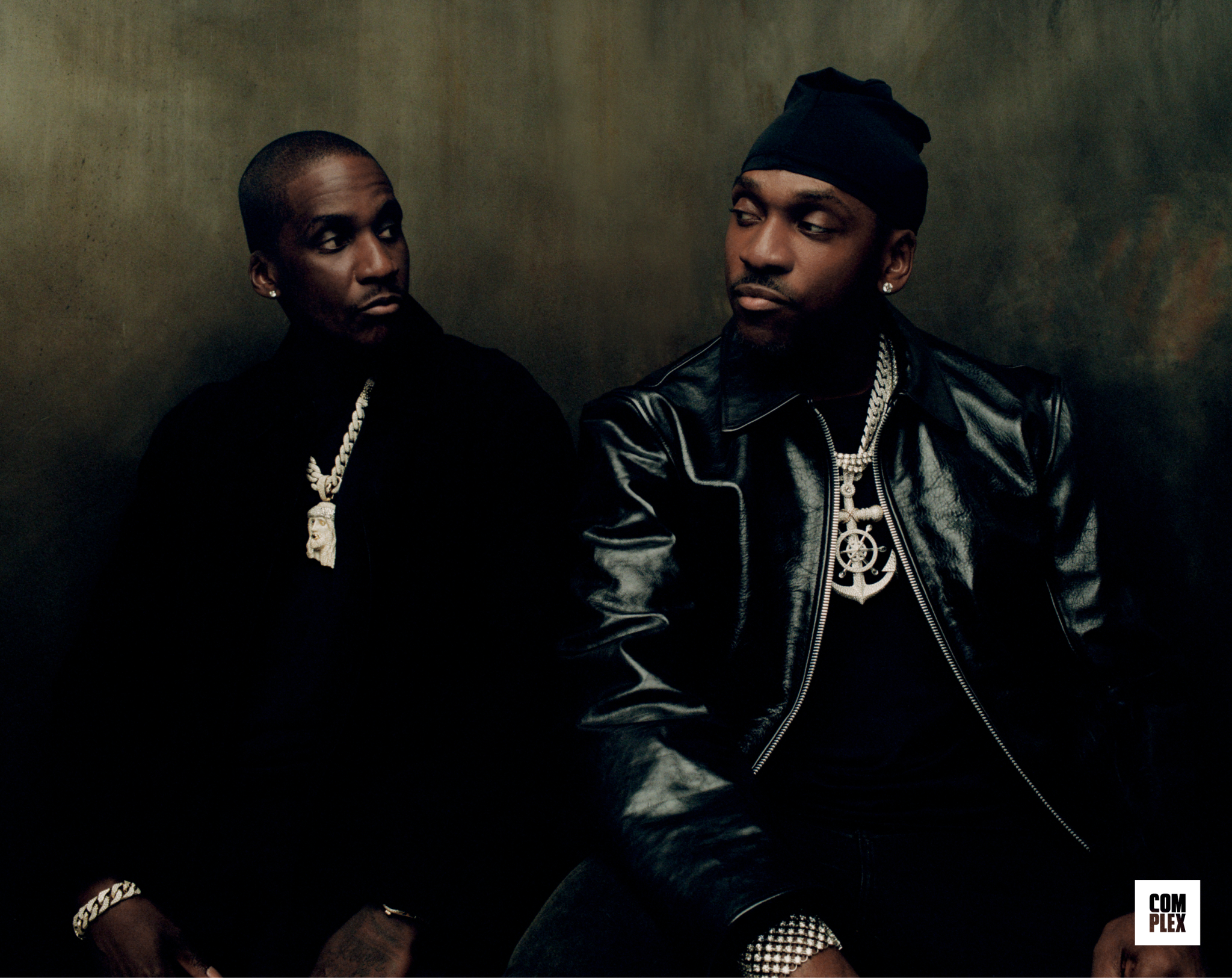 Pusha and Malice from the Clipse sitting side by side, dressed in dark clothing with chains, looking at each other. Complex magazine logo in the corner.