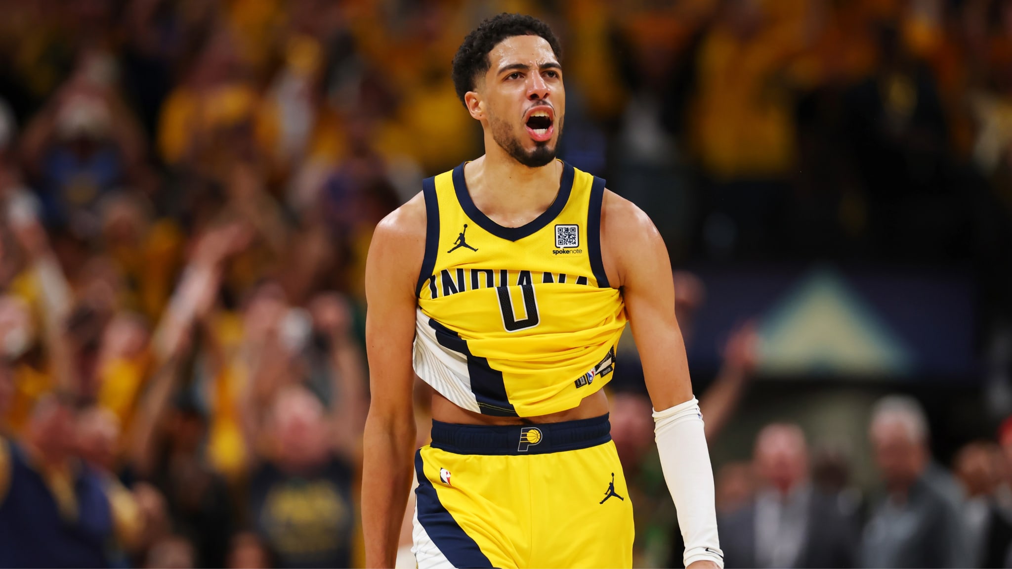 Tyrese Haliburton in a yellow Indiana Pacers jersey, passionately celebrating on the court with a cheering crowd in the background.
