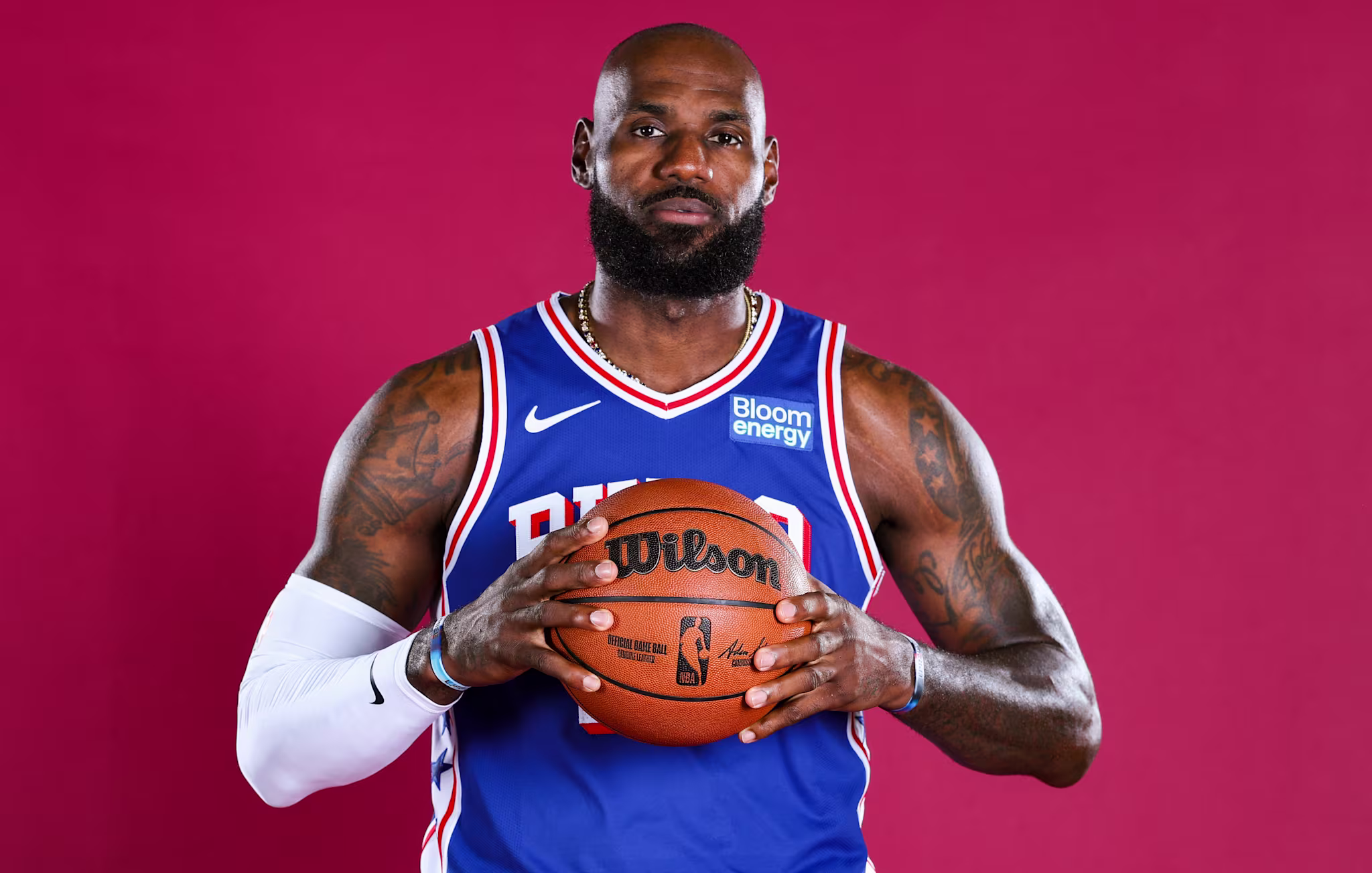 LeBron James in a blue jersey holding a basketball against a red background.