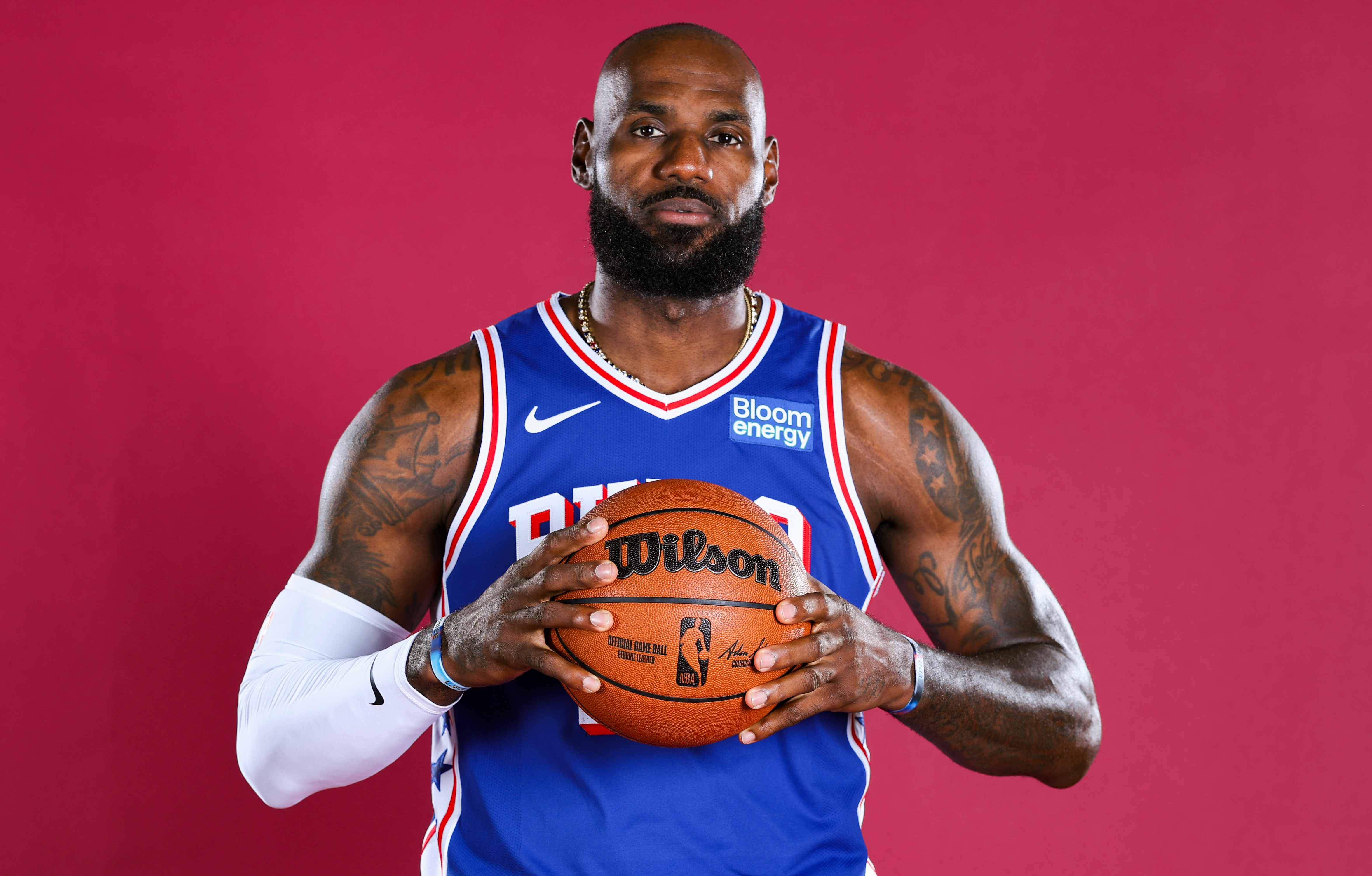 LeBron James in a blue jersey holding a basketball against a red background.