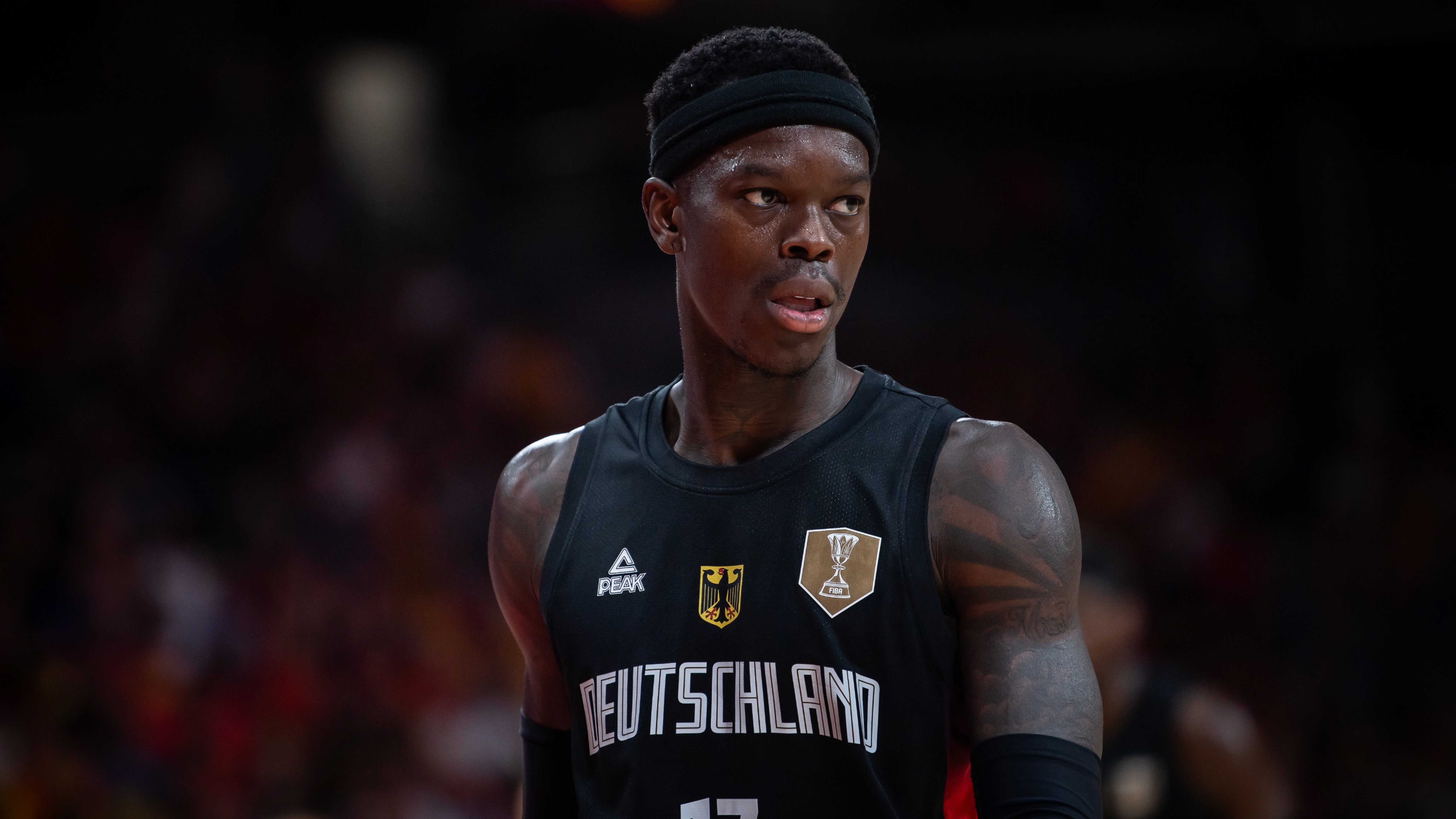 Dennis Schroder in a black "Deutschland" jersey with "17," wearing a headband, on a basketball court.
