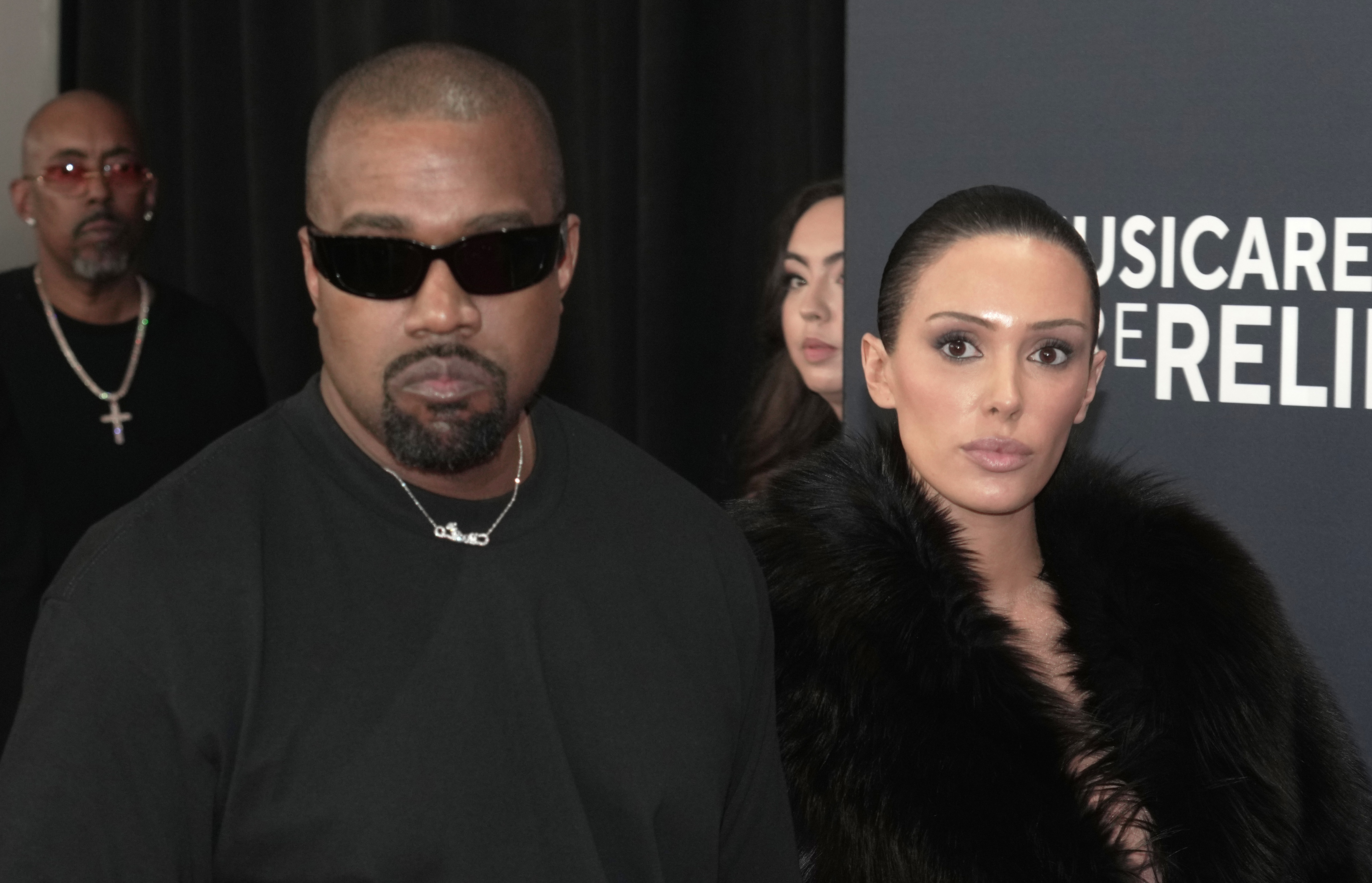 Kanye West in black sunglasses and Bianca Censori in a fur coat at a MusiCares event.