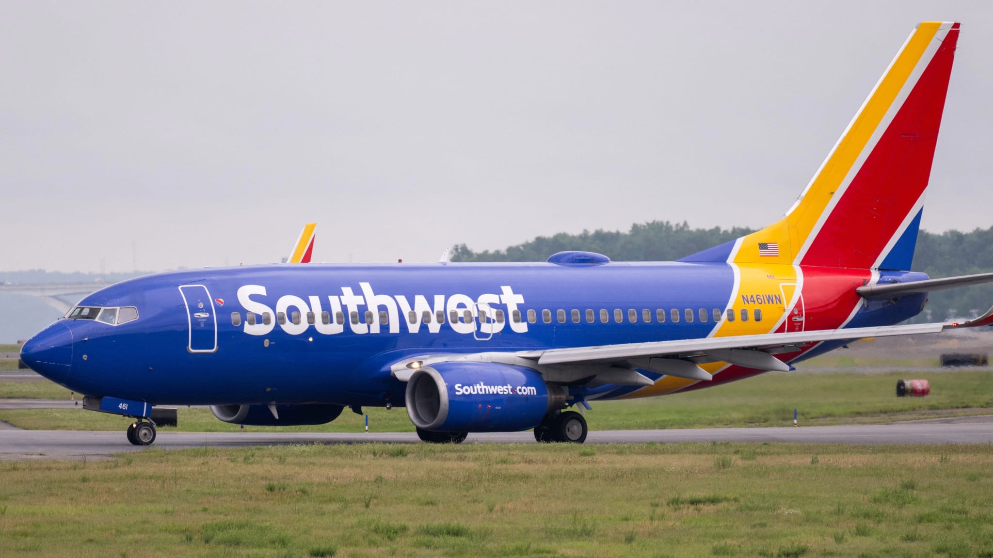 A Southwest Airlines plane on a runway, featuring a blue fuselage with red, yellow, and blue tail design. Grass and trees in the background.