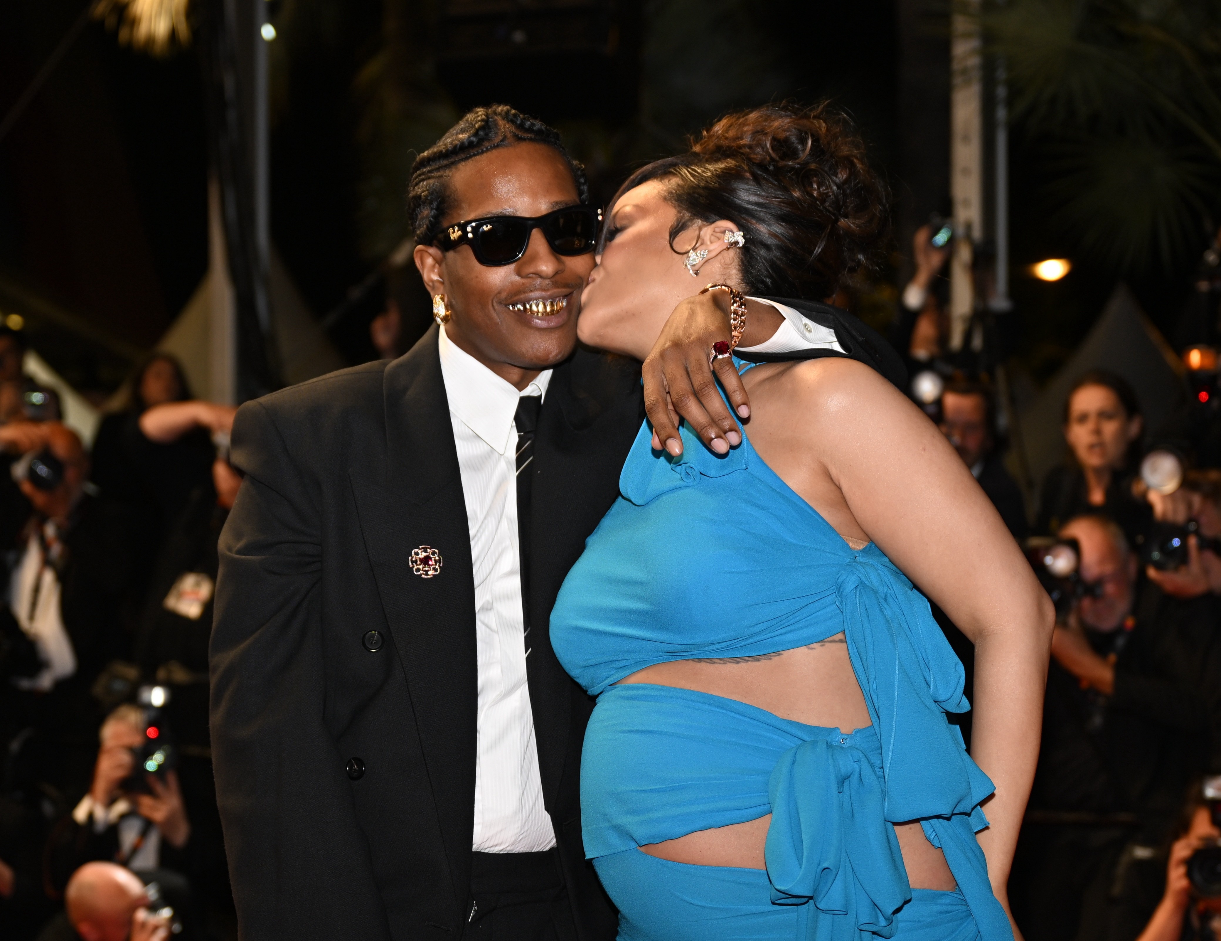 A$AP Rocky and Rihanna at an event, with Rihanna in a blue dress, embracing and smiling.
