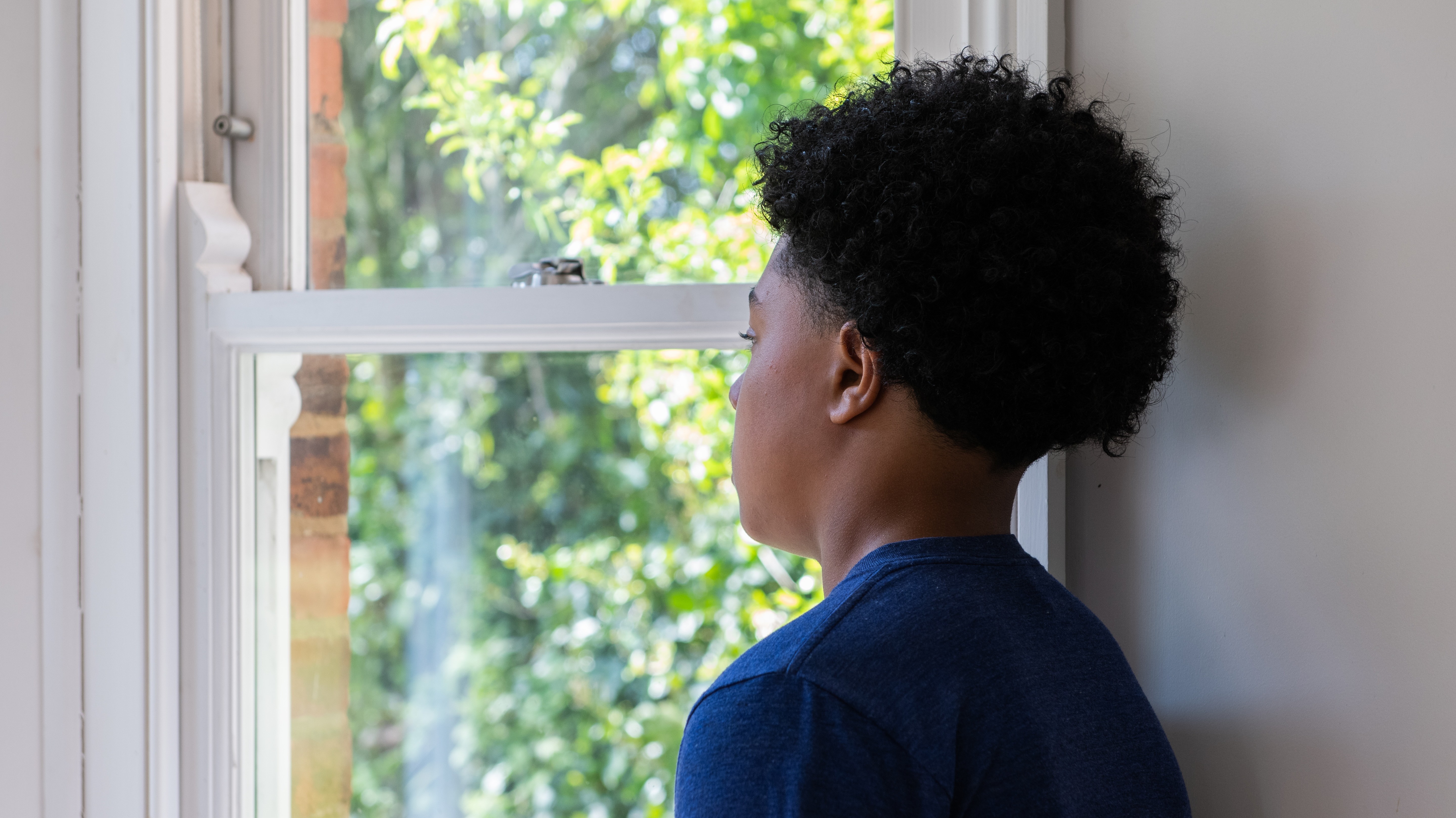 Teenage boy, wearing a blue shirt, looking out of a window
