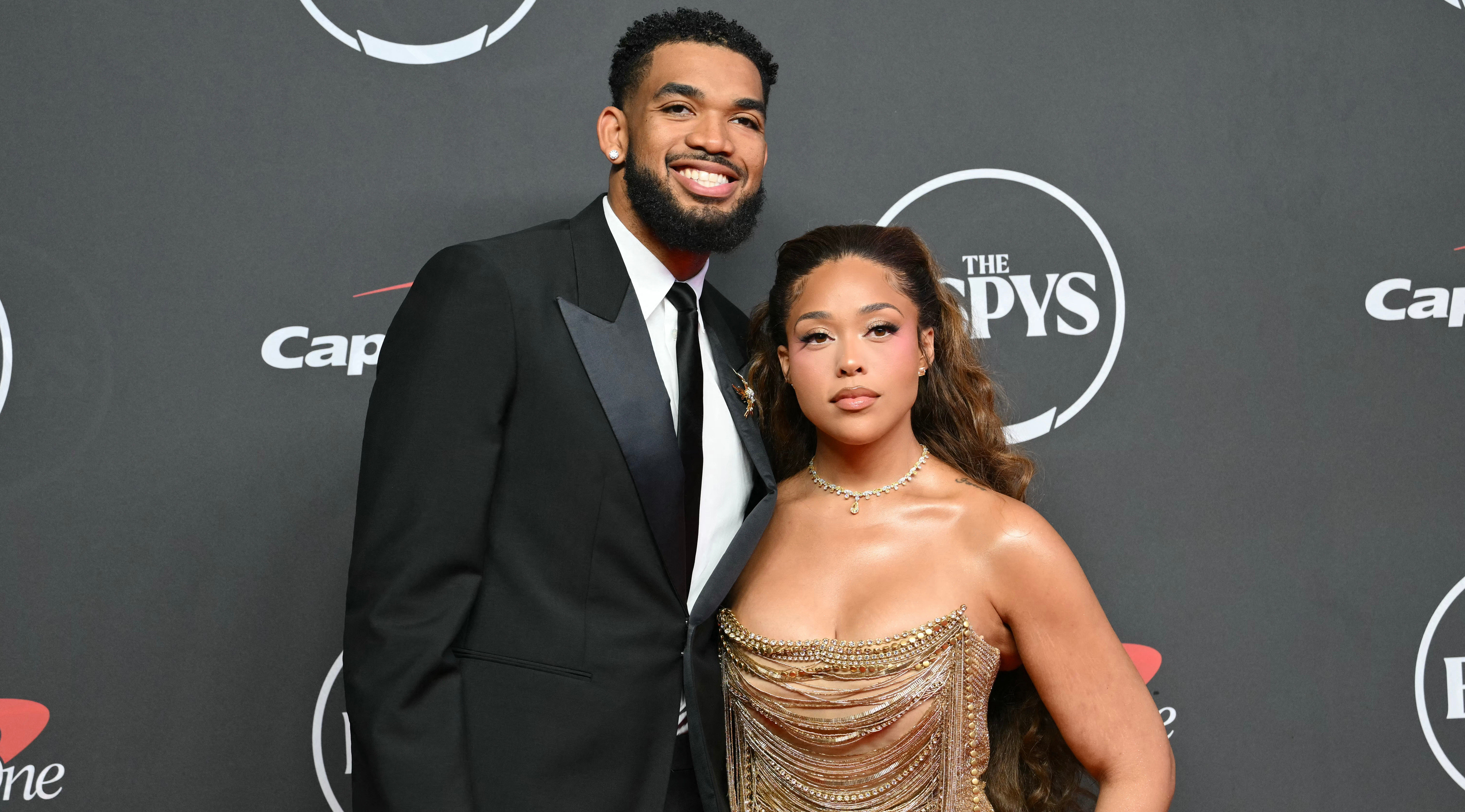 Karl-Anthony Towns in a black tuxedo and Jordyn Woods in a gold dress pose together on the red carpet at the ESPY Awards.