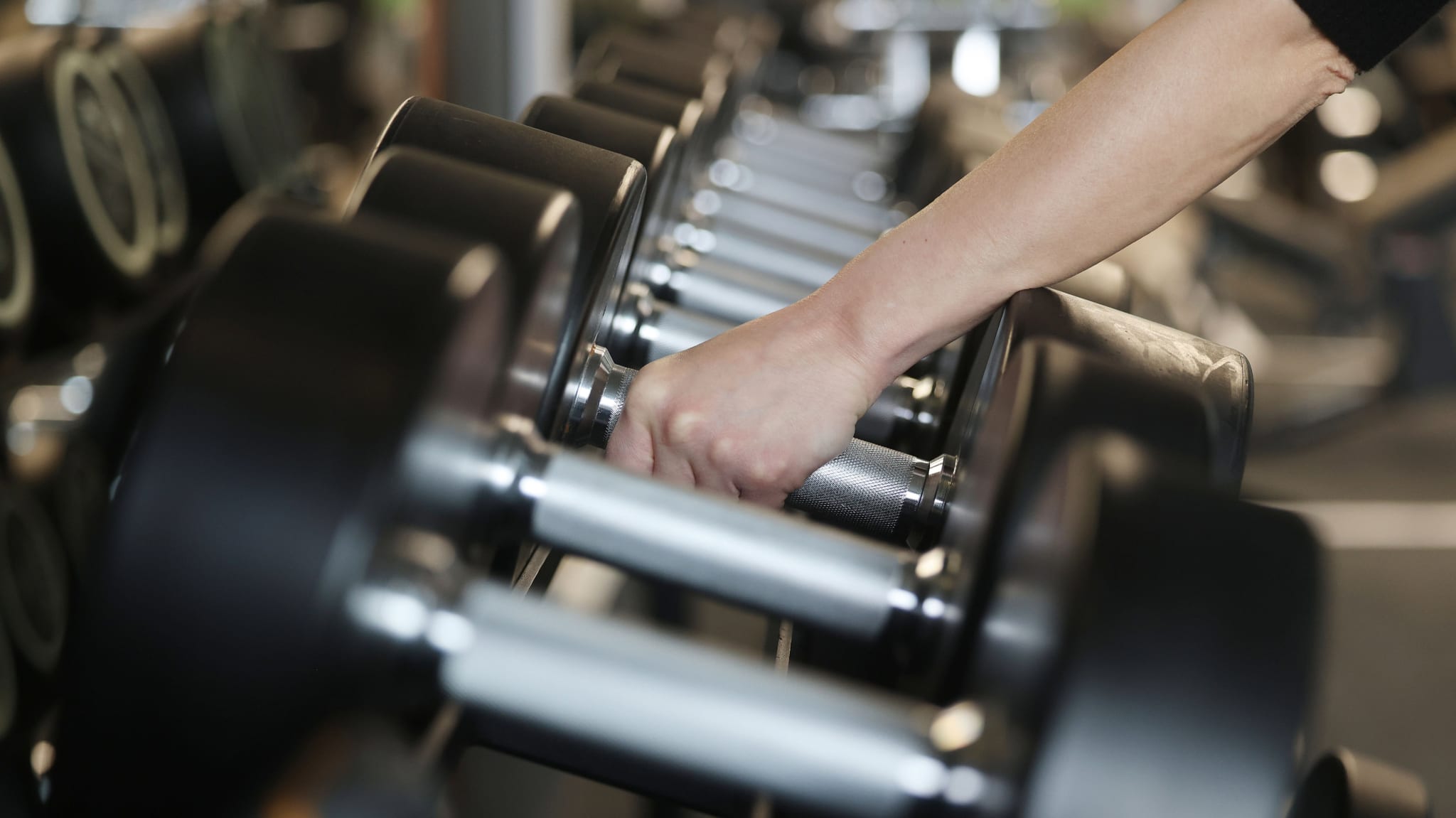 A hand reaching for a dumbbell from a rack in a gym setting.