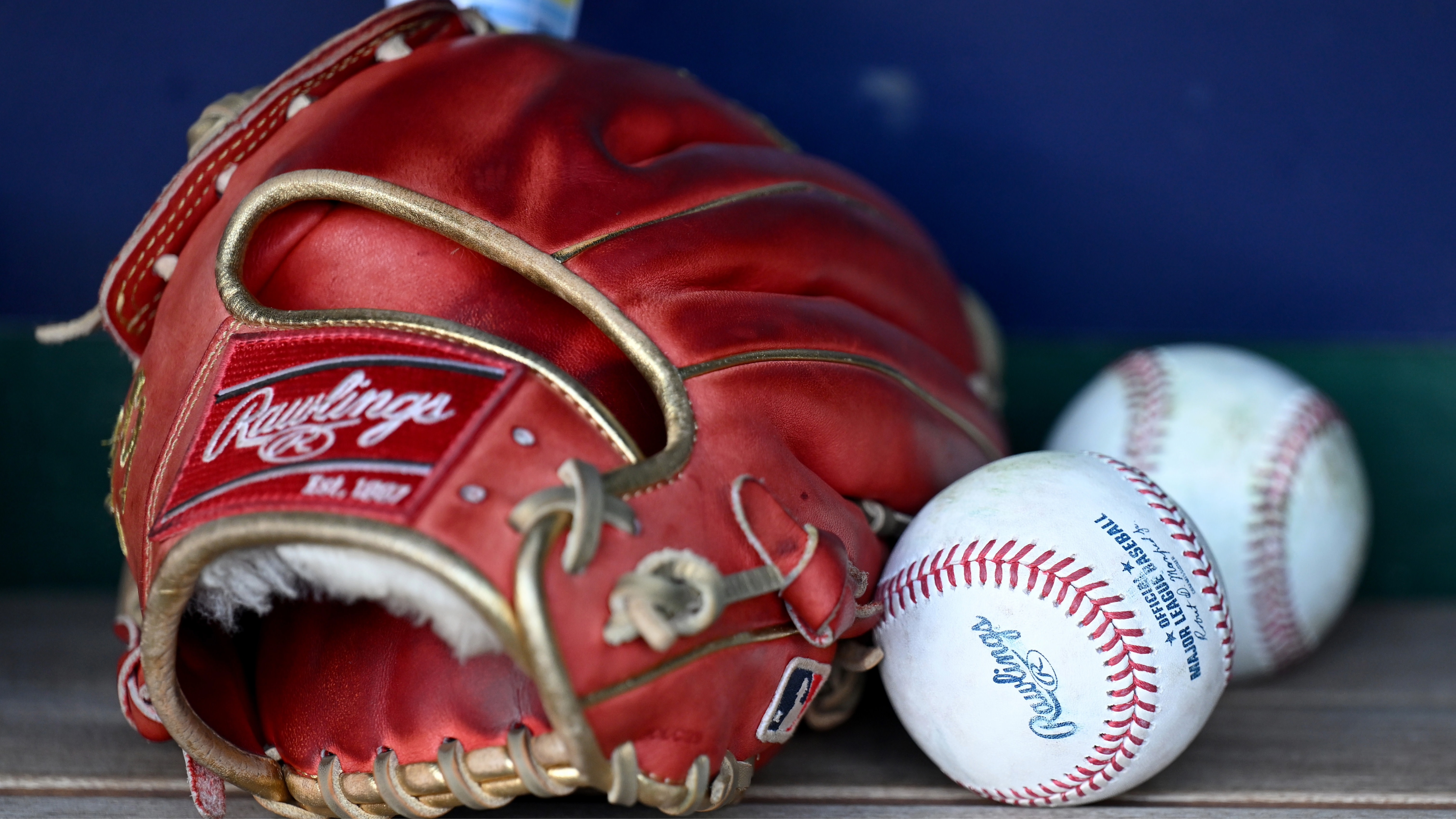 A red baseball glove and two baseballs resting on a wooden bench.