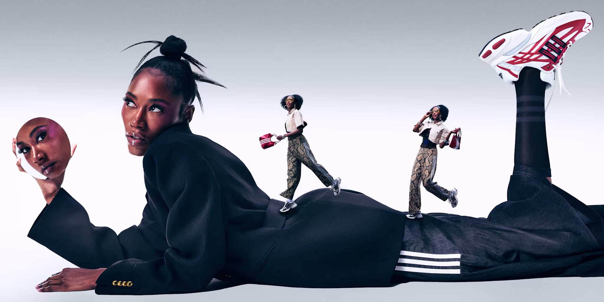 A woman in a black jacket lies down, holding a mask. Miniature versions of herself walk on her back. She wears sneakers with red accents.