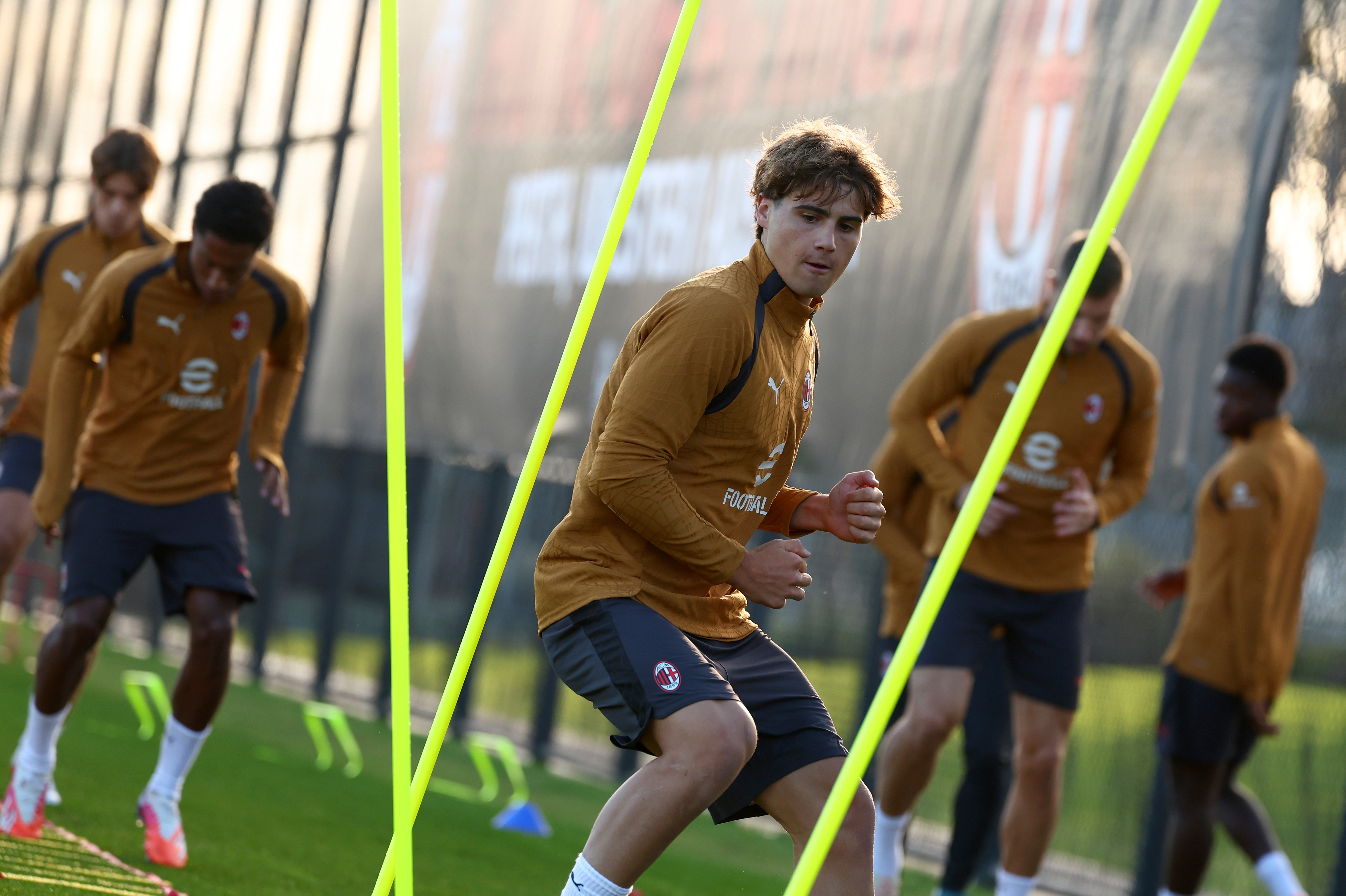 Soccer players in brown training kits practice agility drills on a field, with focus on one player in the foreground.