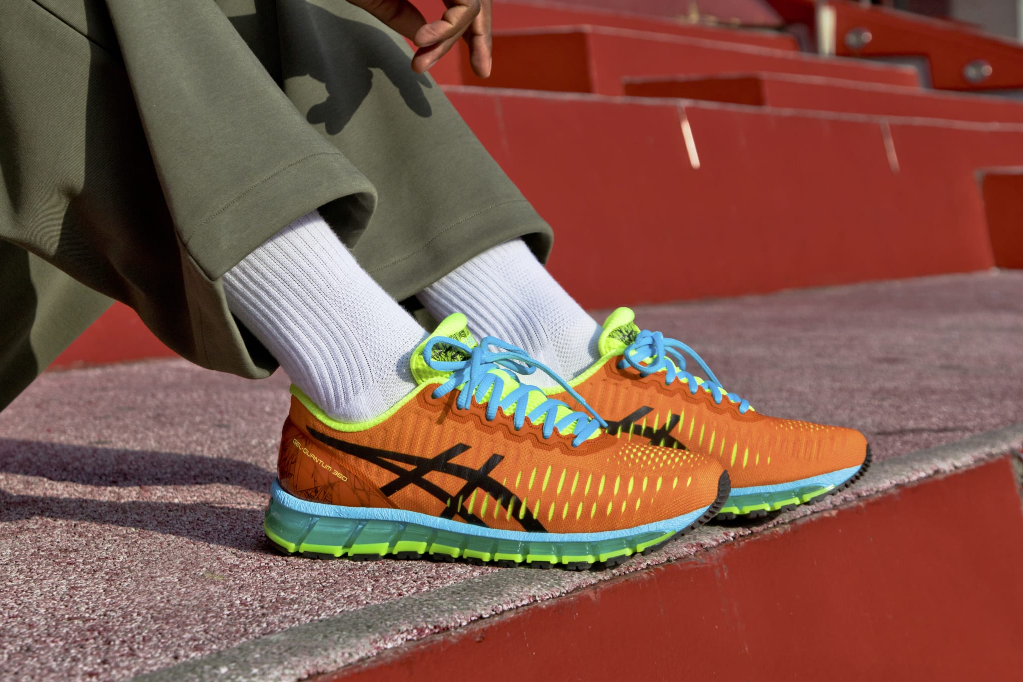 Person sitting on red steps wearing orange Asics sneakers with green and blue accents, white socks, and green pants.