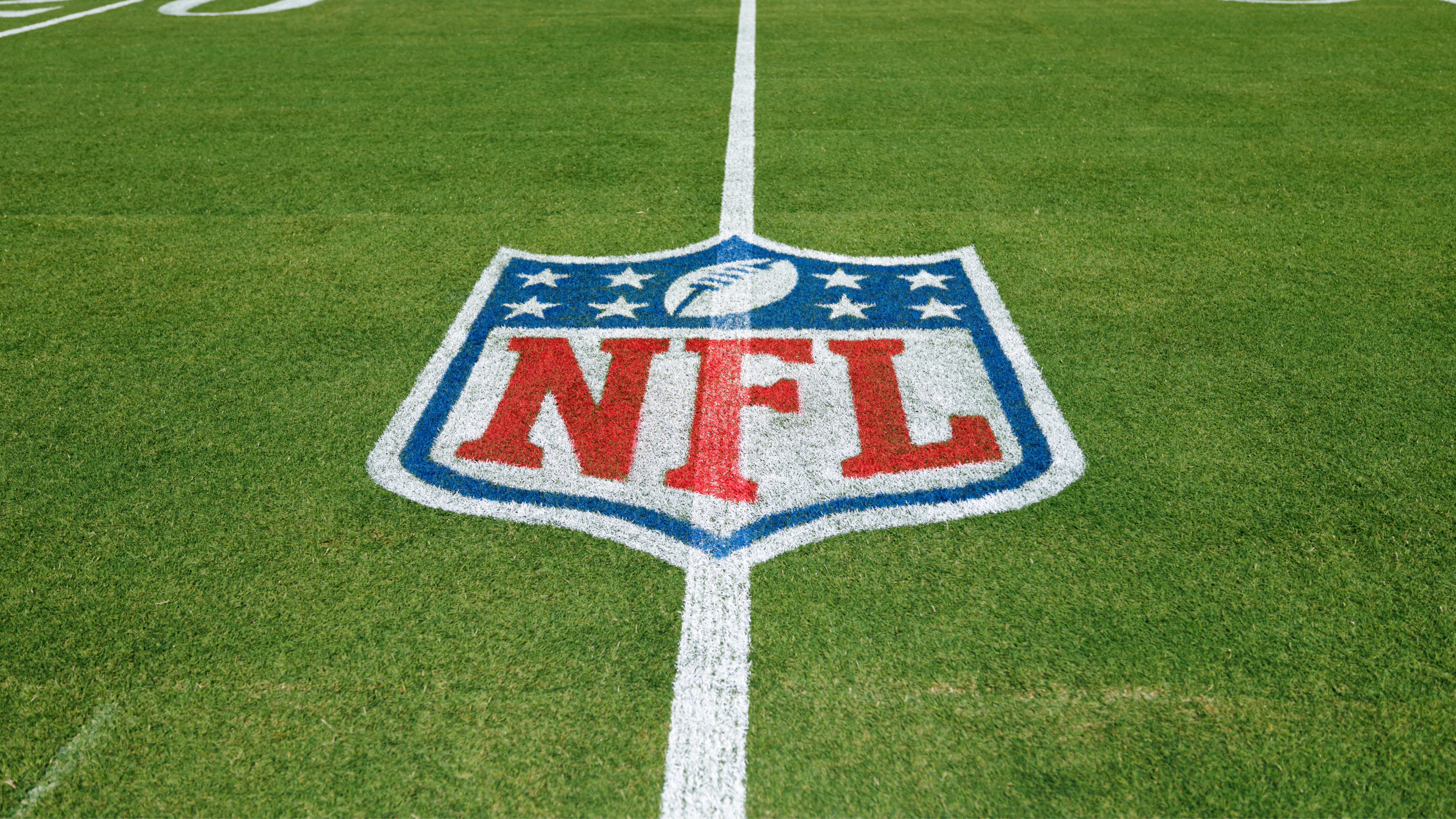 NFL logo painted on a football field's green grass, centered on a white yard line.