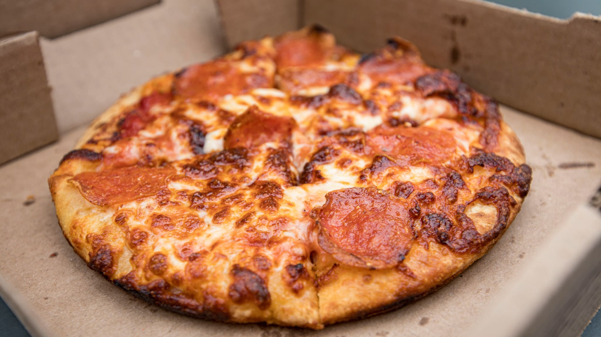 A pepperoni pizza with melted cheese and crispy edges in an open cardboard box.
