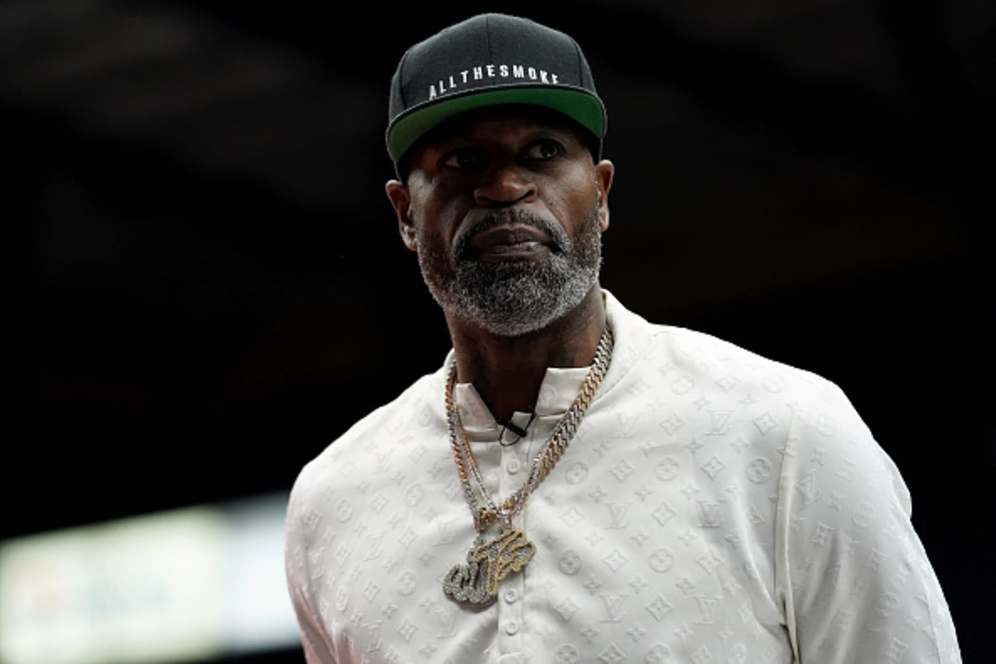 Stephen Jackson wearing a black "ALL THE SMOKE" cap, a white patterned shirt, and gold chains, looking to the side.