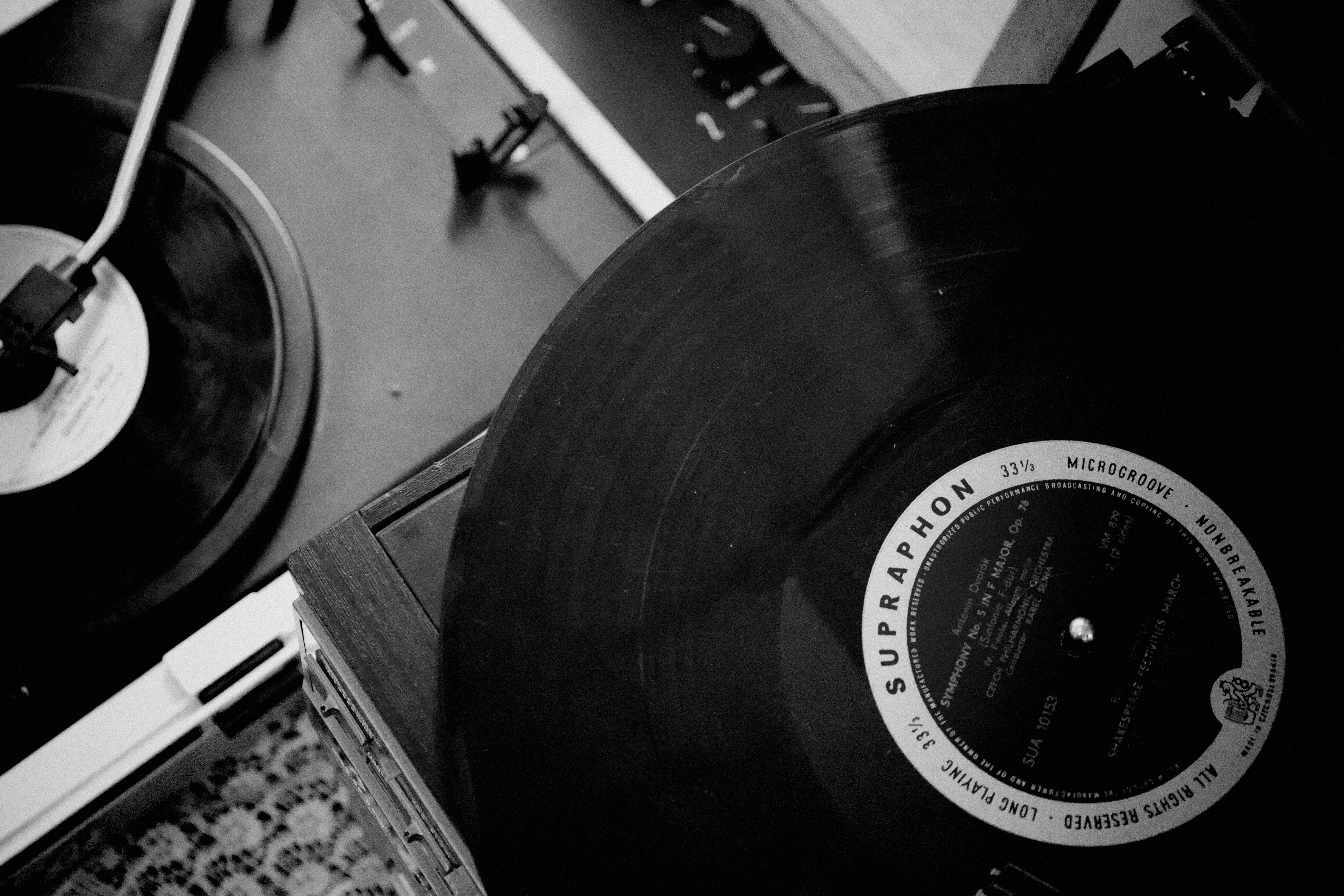 A black and white image of a turntable playing a vinyl record labeled "Supraphon." Another record is partially visible on a second turntable.