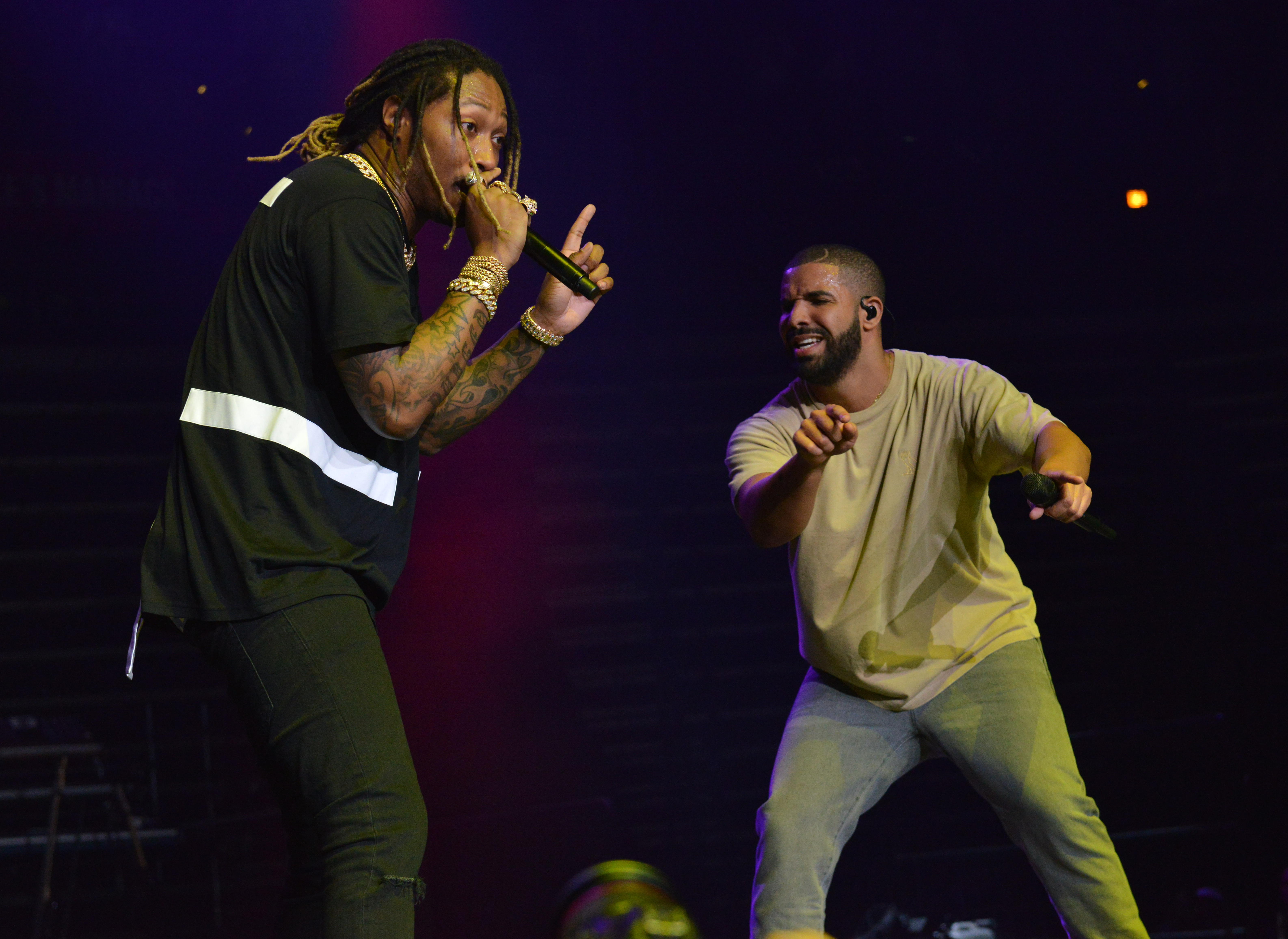 Future and Drake performing on stage. Future holds a microphone, wearing a black shirt with white stripes. Drake points, wearing a beige shirt.