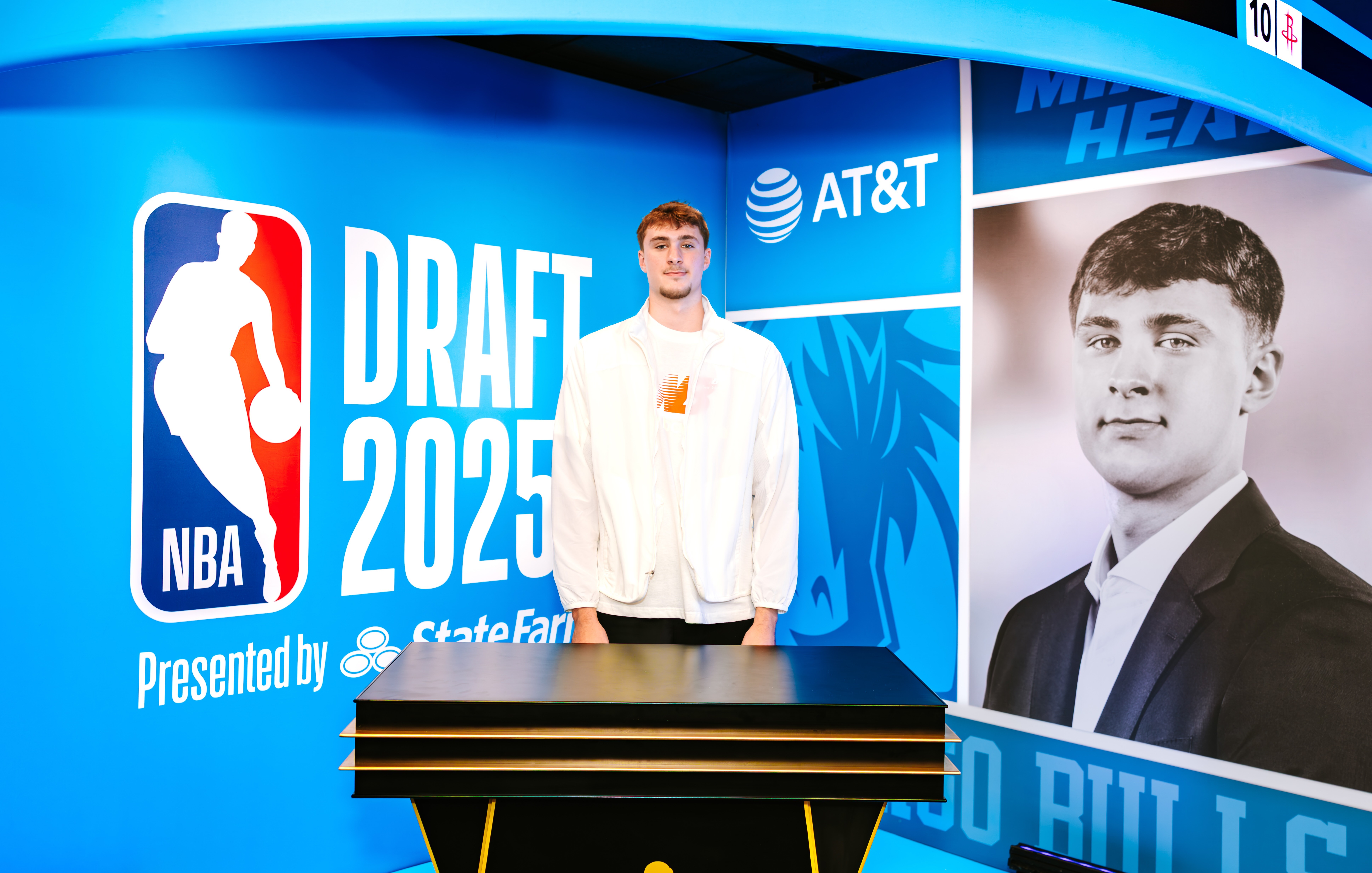 Cooper Flagg at the NBA Draft 2025 event, beside a large backdrop with logos and his portrait.