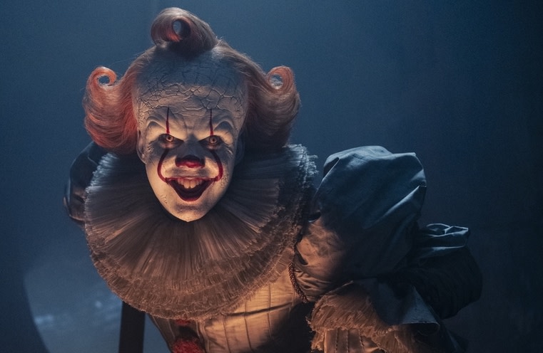 Pennywise the clown from "It," with a menacing smile, in a dimly lit setting.