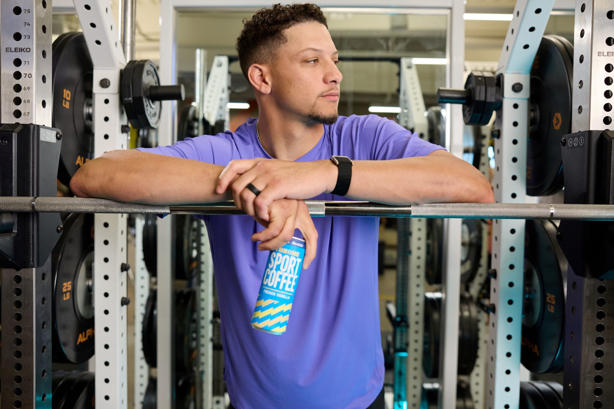 Patrick Mahomes leans on a barbell rack, holding a can labeled "Throne Sport Coffee."