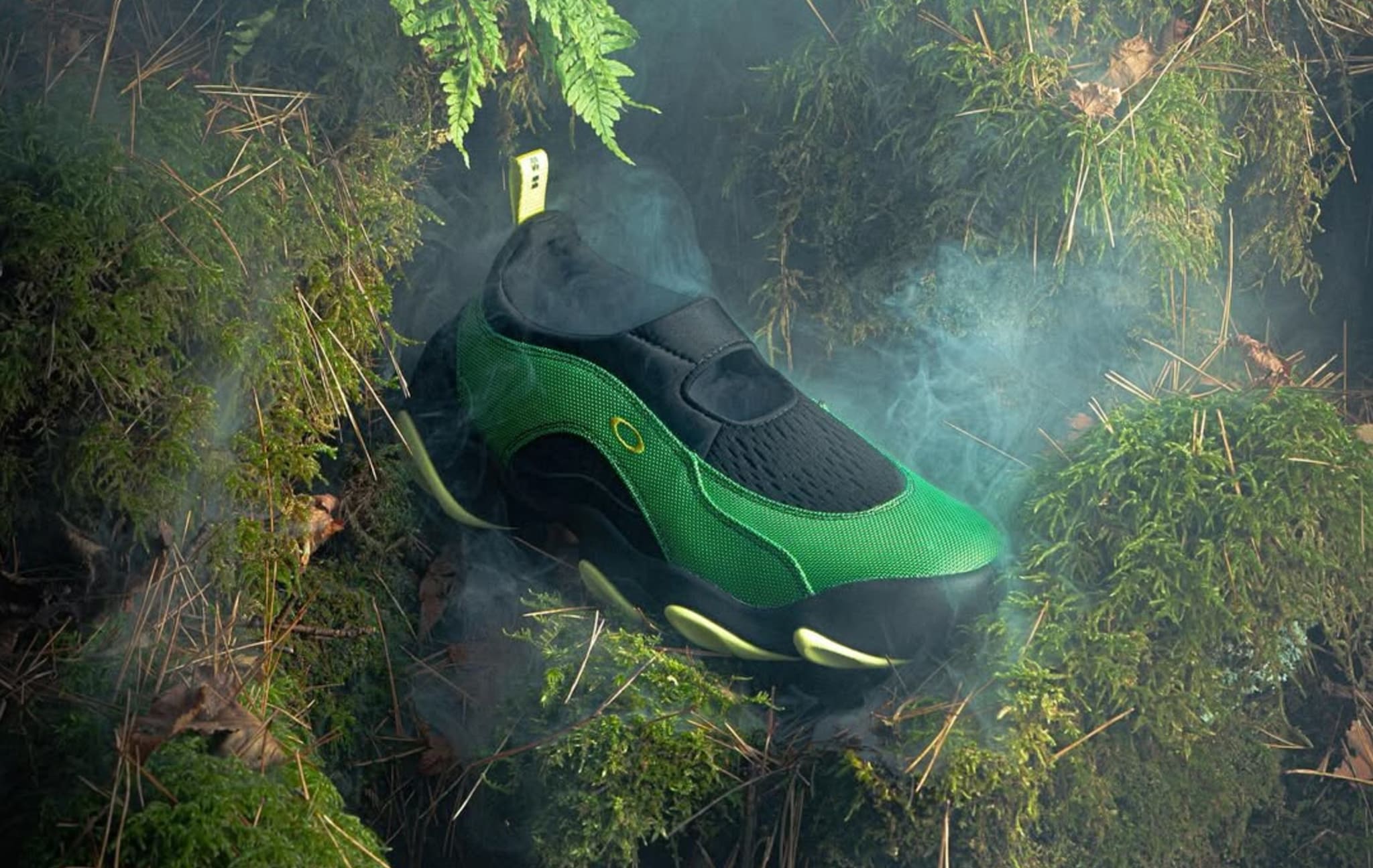 A green and black shoe with a sleek design rests on moss-covered ground, surrounded by misty fog and ferns.