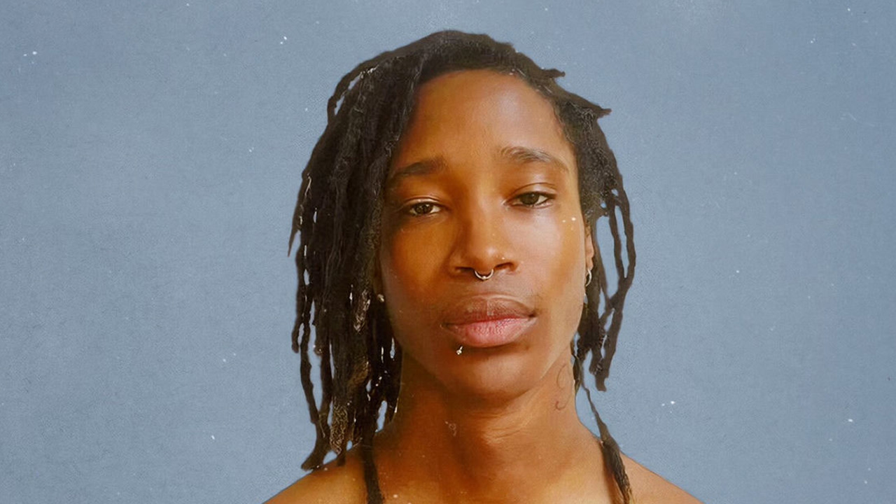 Person with dreadlocks and a septum piercing against a plain background.